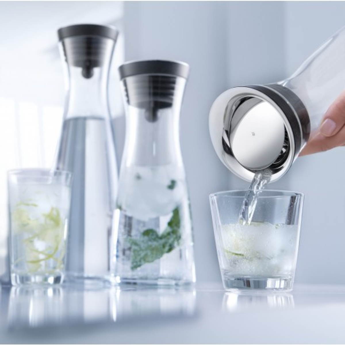 Gießen von Wasser aus einer Kanne in ein Glas mit Limette.