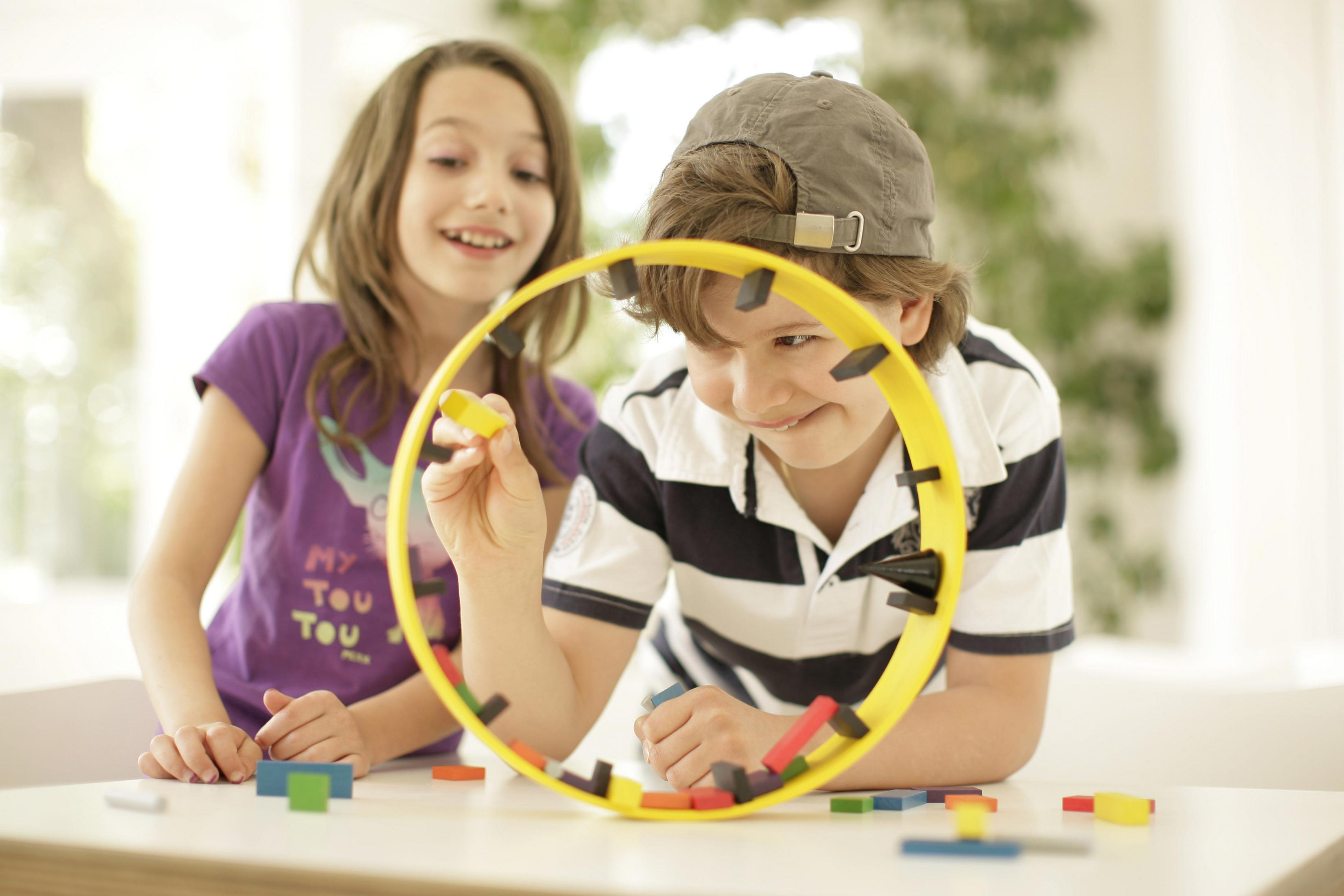 Zwei Kinder spielen mit einem gelben Ring mit bunten Teilen darin.