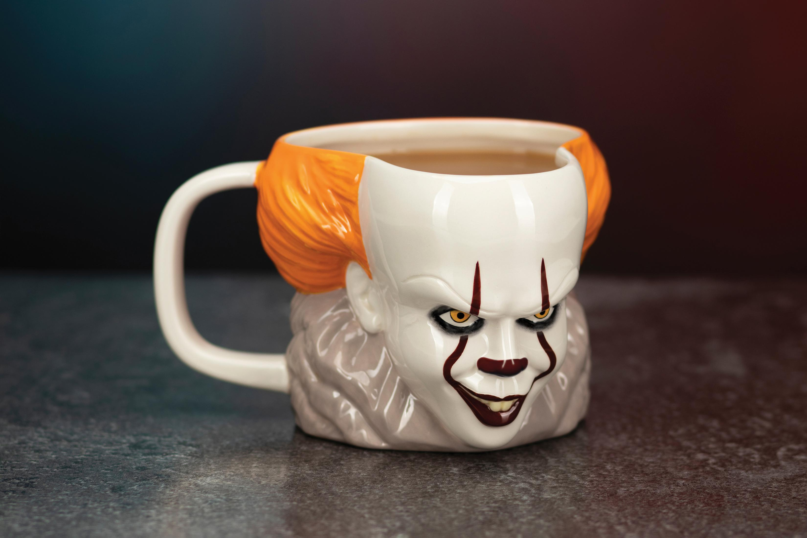 Pennywise-Tasse mit orangefarbenem Haar und weißem Gesicht, mit dunklem, verschwommenem Hintergrund.