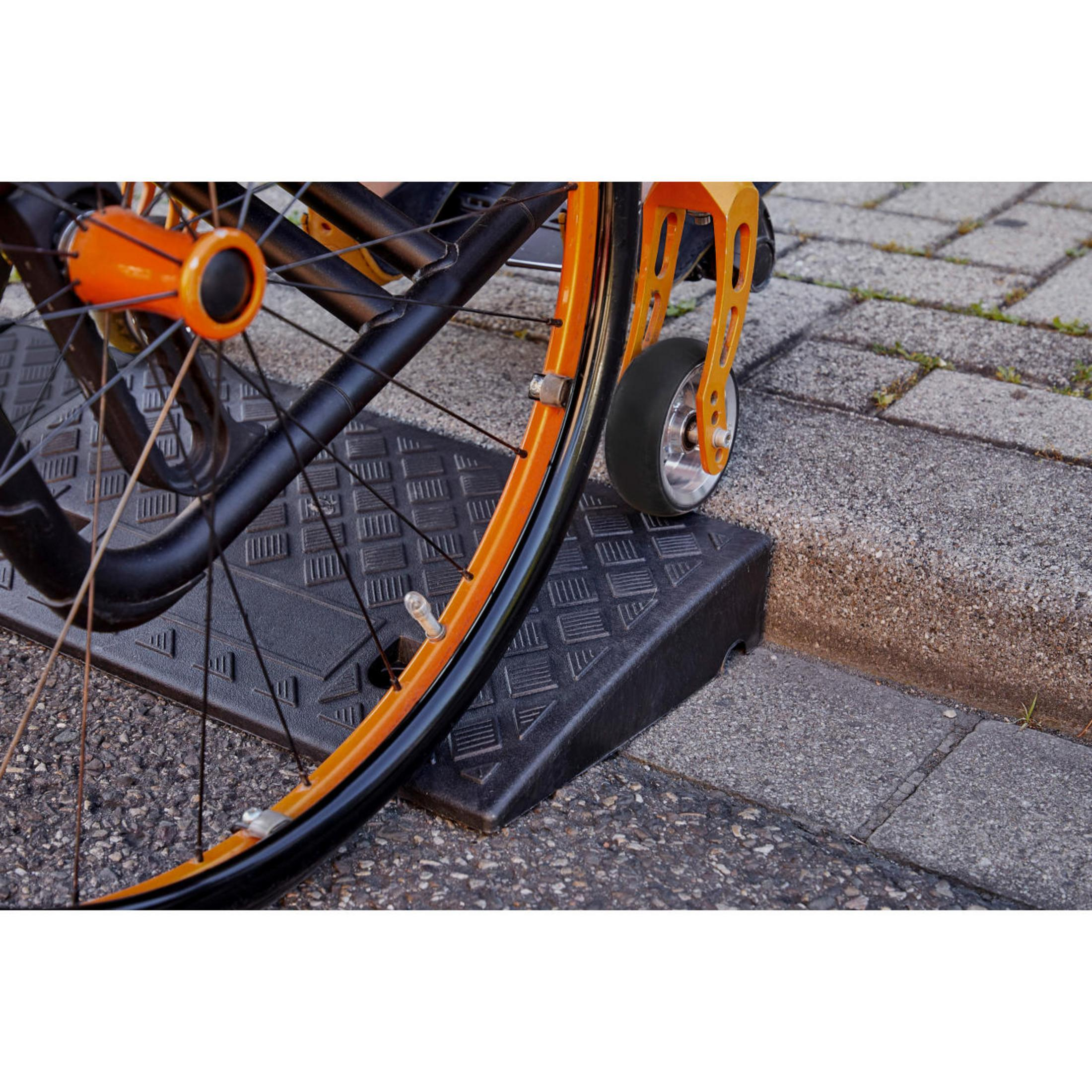Rollstuhlrad auf einer Rampe, um einen Bordstein zu überwinden. Schwarze Rampe, orangefarbenes Rad.