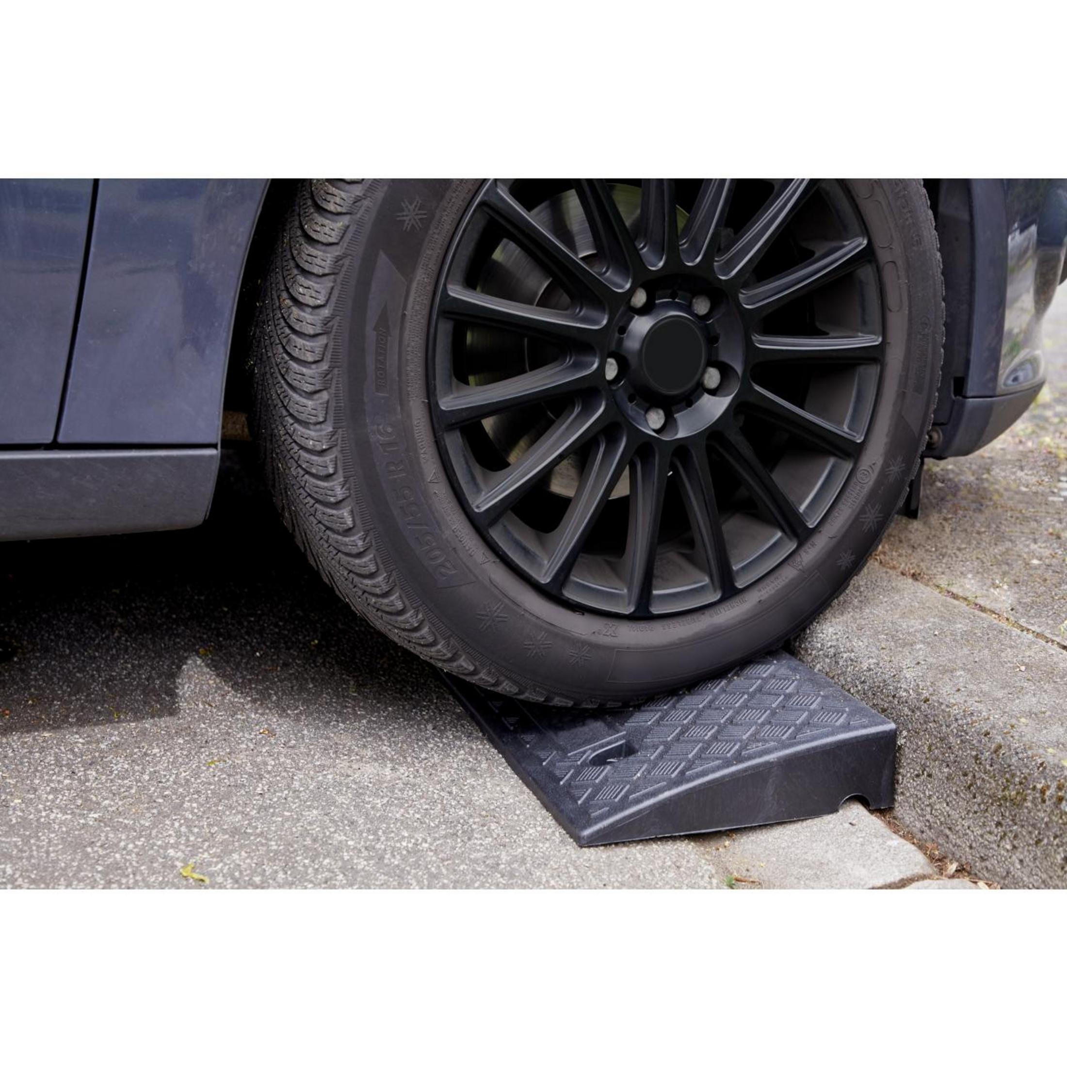 Ein Autoreifen steht auf einer schwarzen Rampe auf einem Bürgersteig. Der Hintergrund ist Beton.