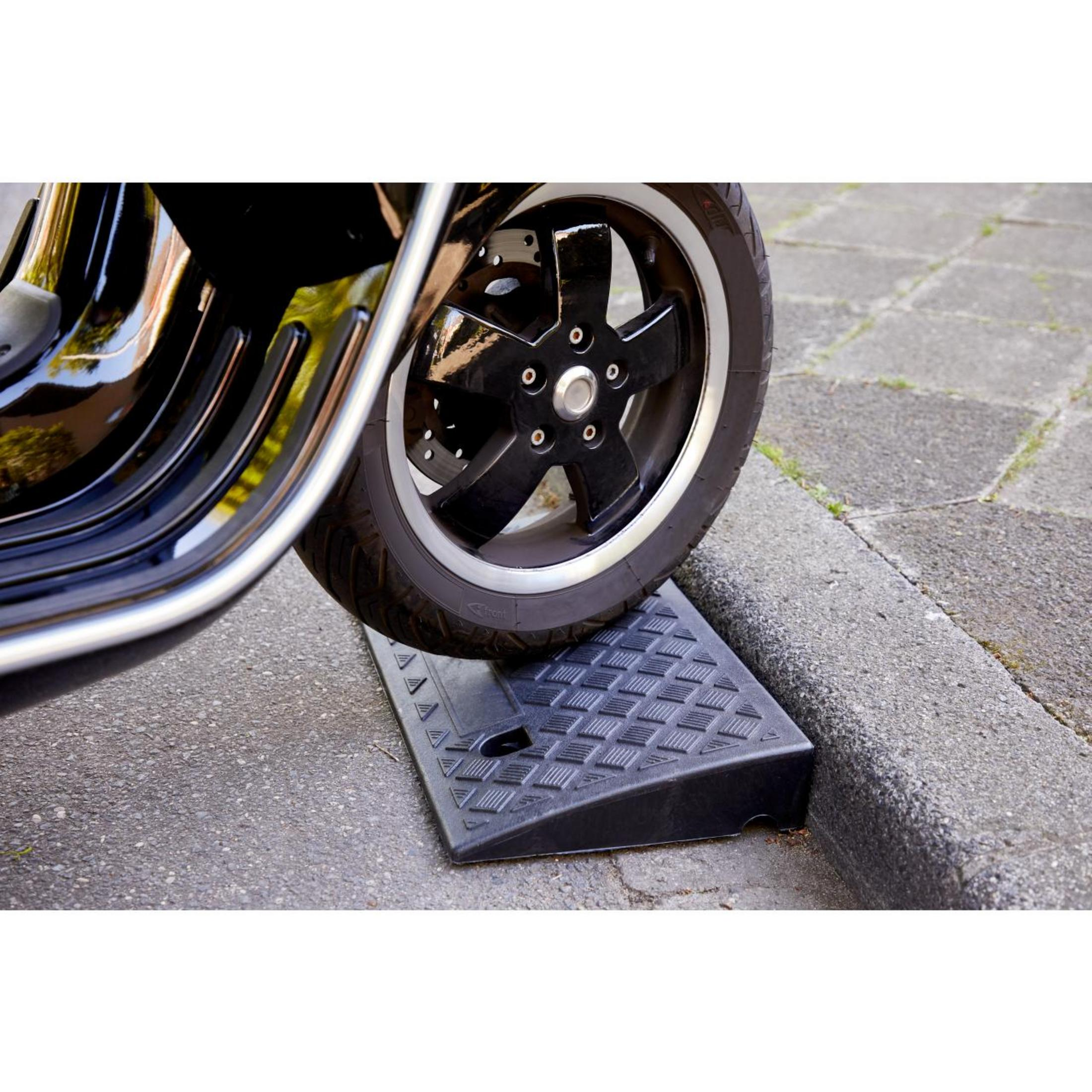 Motorradreifen auf Rampe. Schwarzer Reifen auf schwarzer Rampe. Grauer Asphalt im Hintergrund.