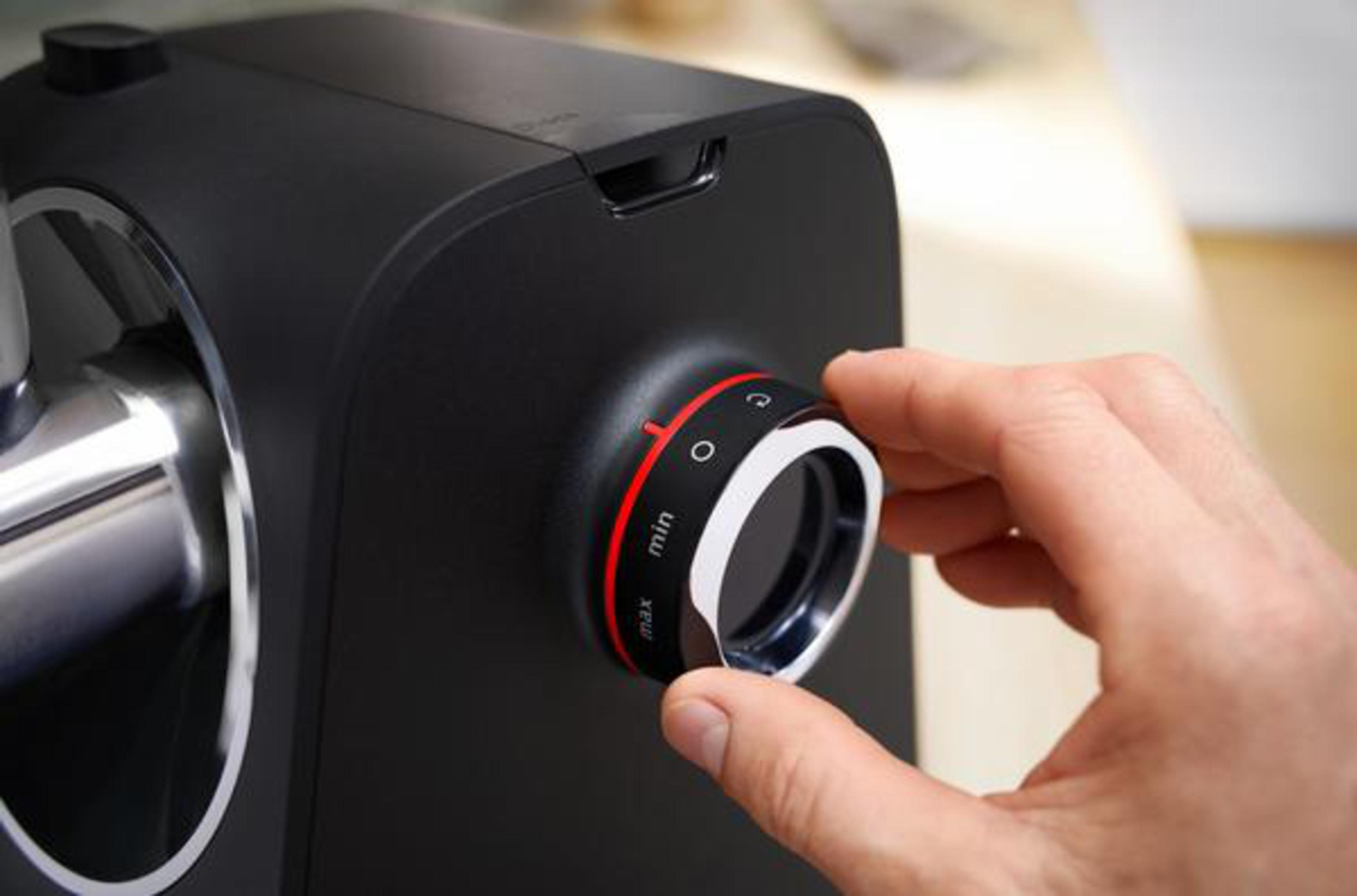 Ręka reguluje pokrętło czarnego urządzenia. Pokrętło ma czerwone oznaczenia i chromowaną obwódkę.