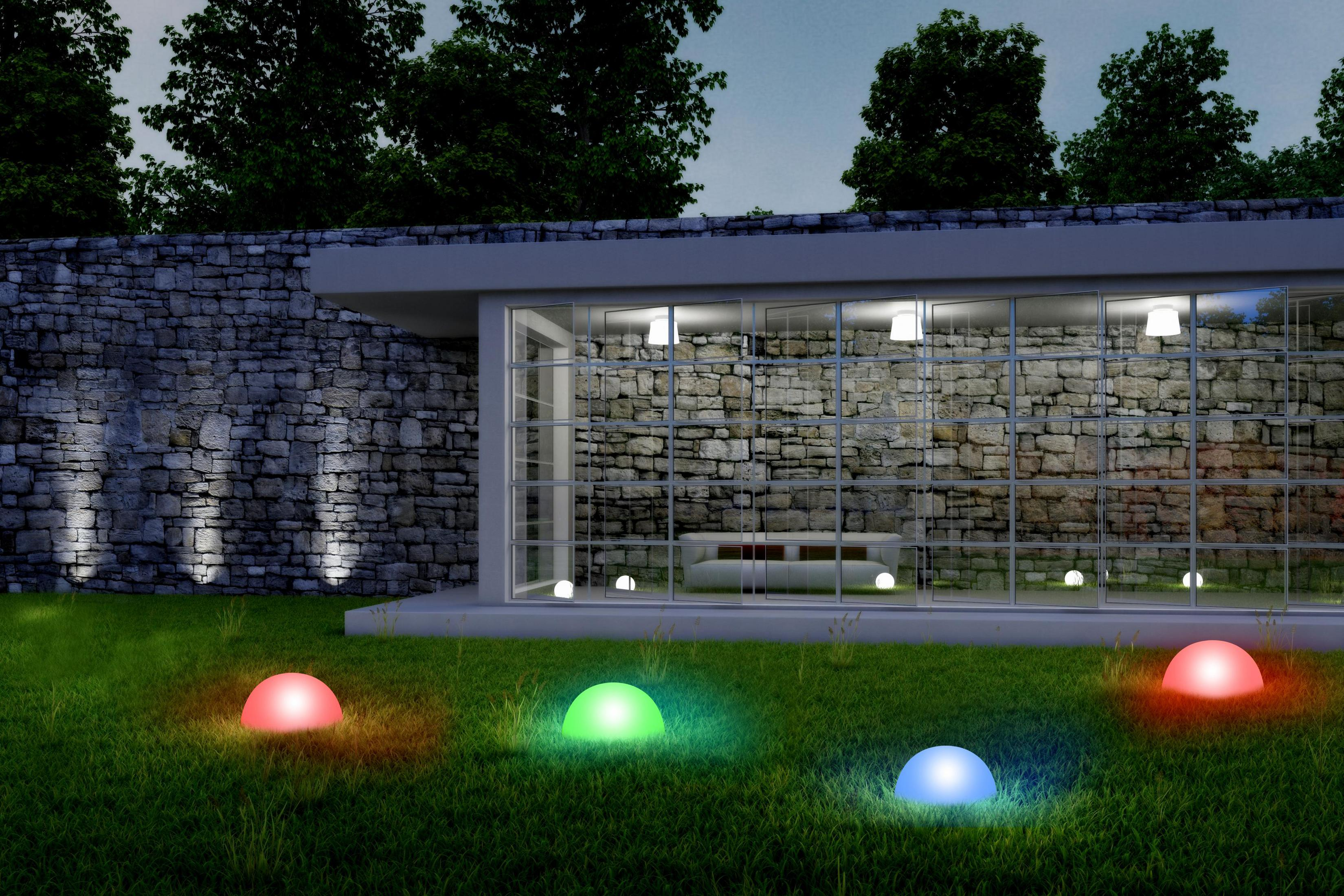 Jardin illuminé avec des lumières colorées. Un bâtiment avec des lumières à l'intérieur et un mur en pierre. Herbe verte.
