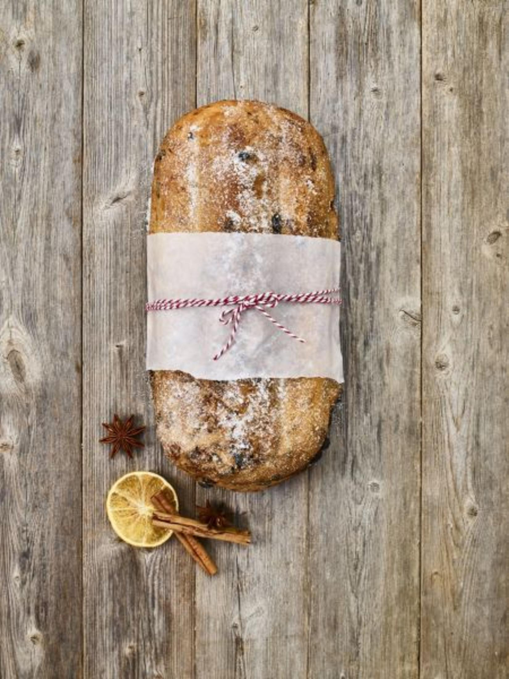 Ein verpacktes, dekoriertes Brotlaib auf Holz. Sternanis, Zimtstangen und eine Zitronenscheibe liegen daneben.