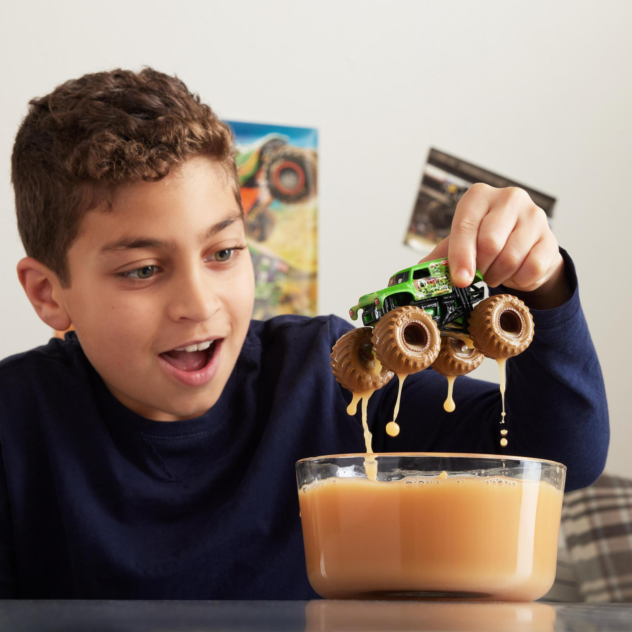 Junge hält einen Spielzeug-Monstertruck über einer Schüssel, aus der Flüssigkeit tropft.