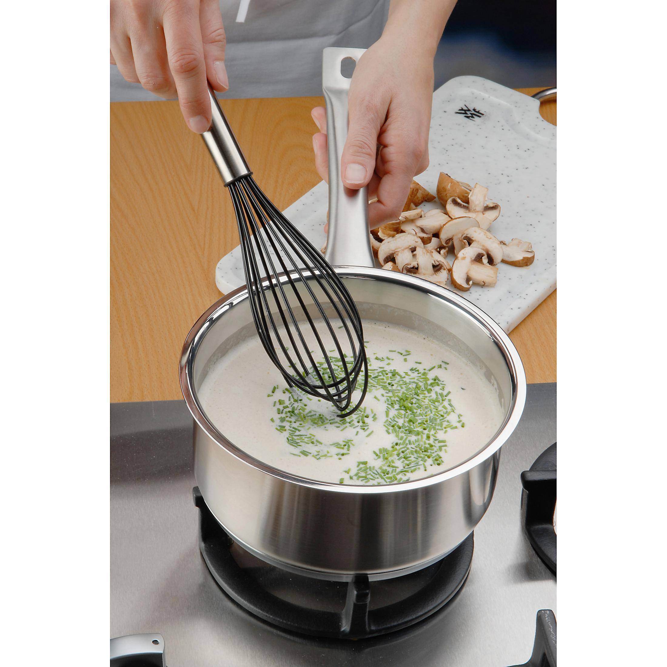 Osoba ubija w garnku. Szczypiorek i grzyby z boku. Na kuchence. Gotowanie w kuchni.