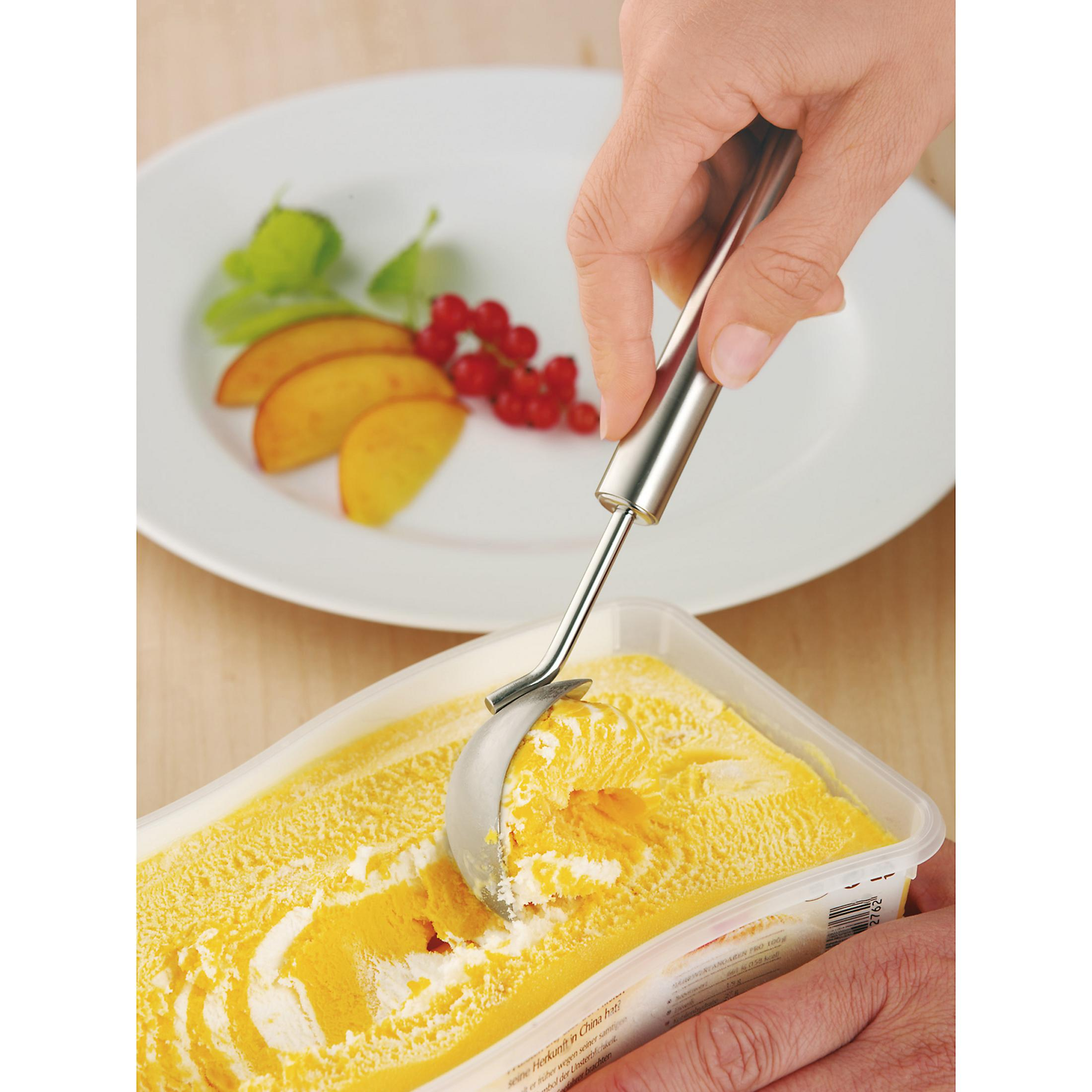 Eine Hand, die mit einem Metalllöffel gelbes Eis aus einem Behälter schöpft. Weißer Hintergrund.