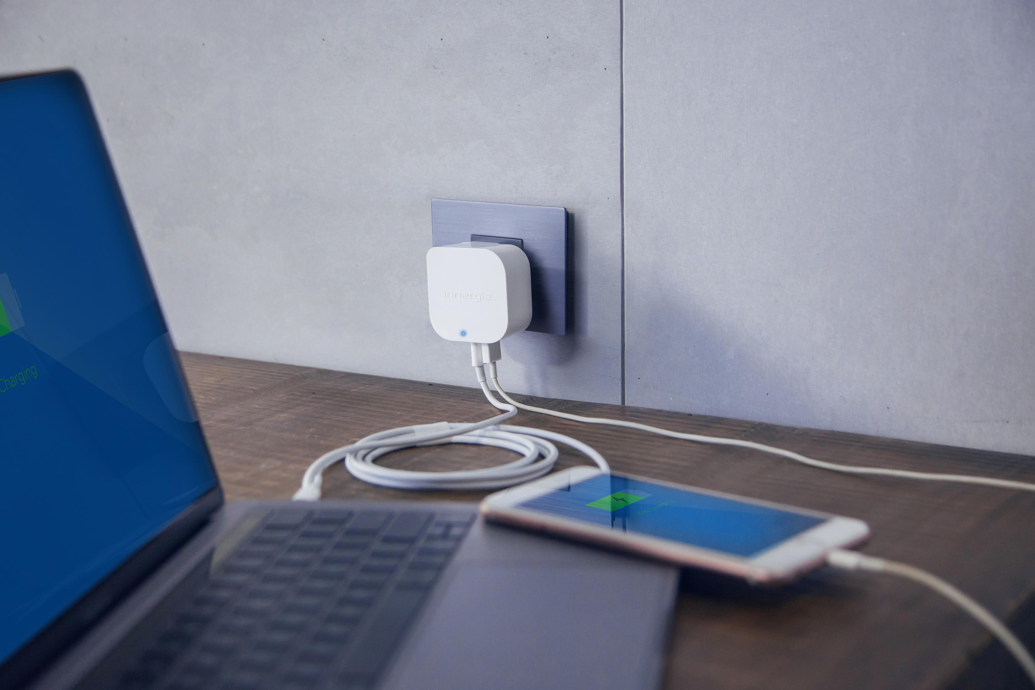 Laptop und Telefon laden auf einem Holzschreibtisch über ein weißes Ladegerät, das an eine Steckdose angeschlossen ist.
