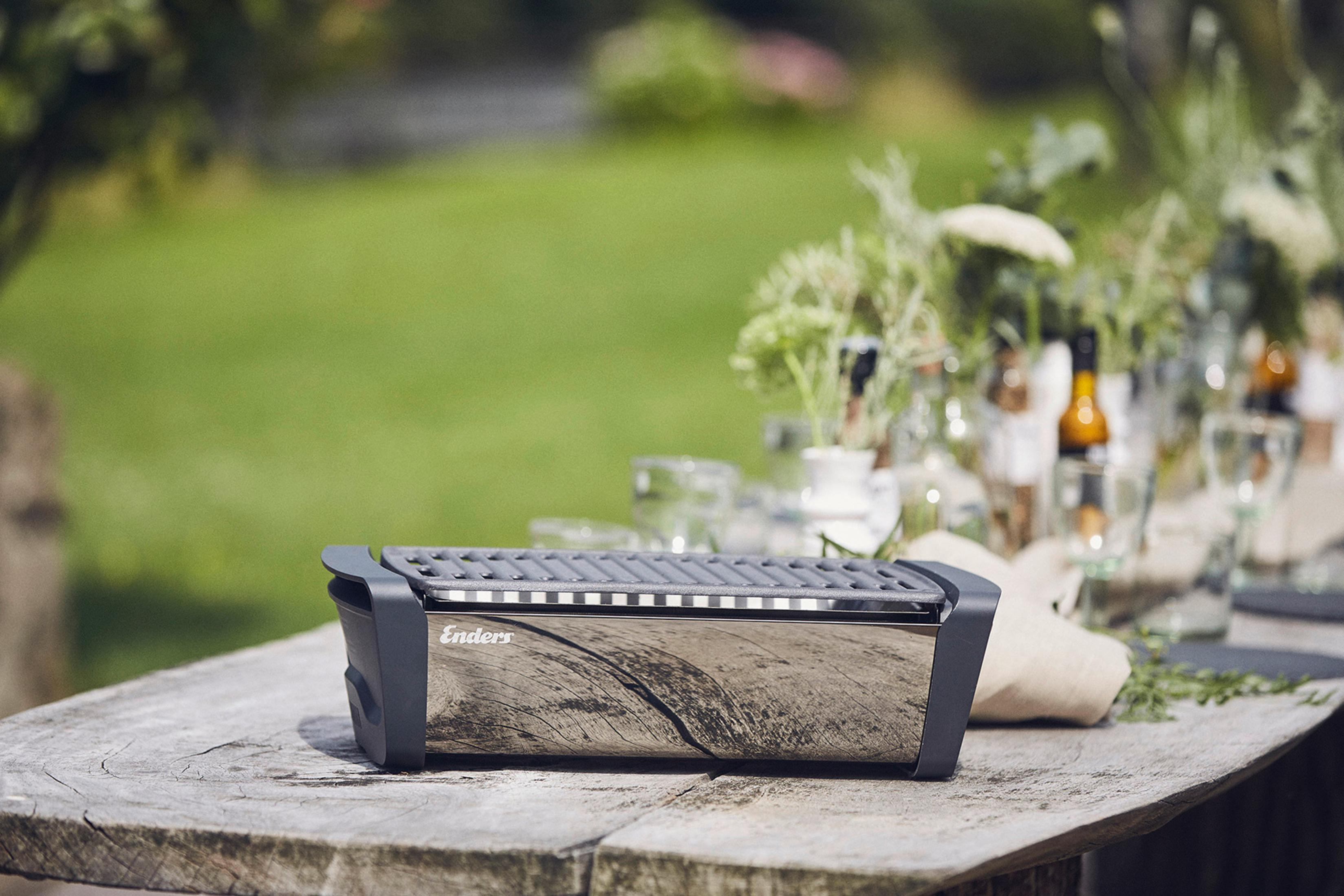 Silberner Grill auf Holztisch, verschwommener grüner Hintergrund im Freien.