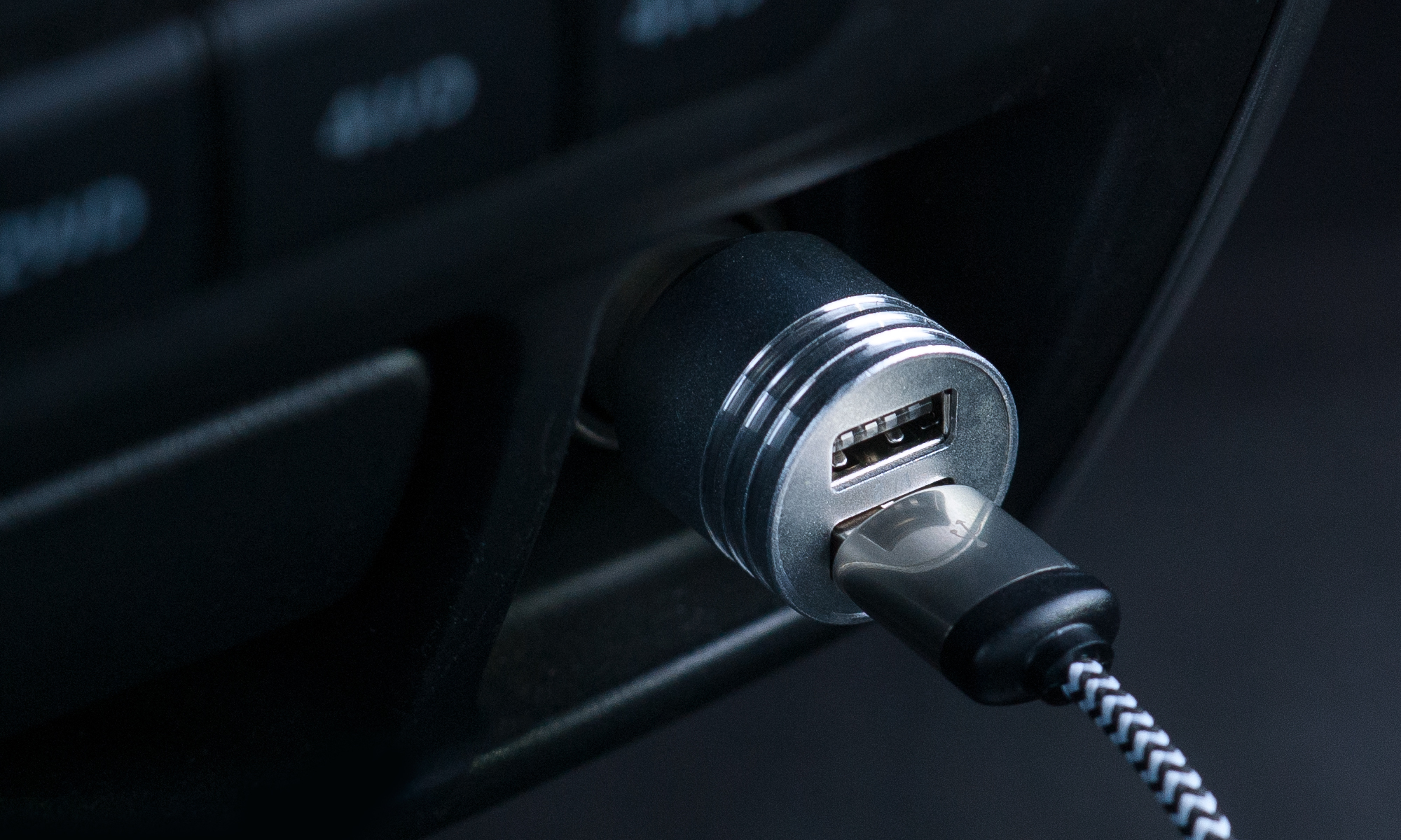 Caricatore USB per auto collegato, primo piano, interni neri, cavo a strisce.