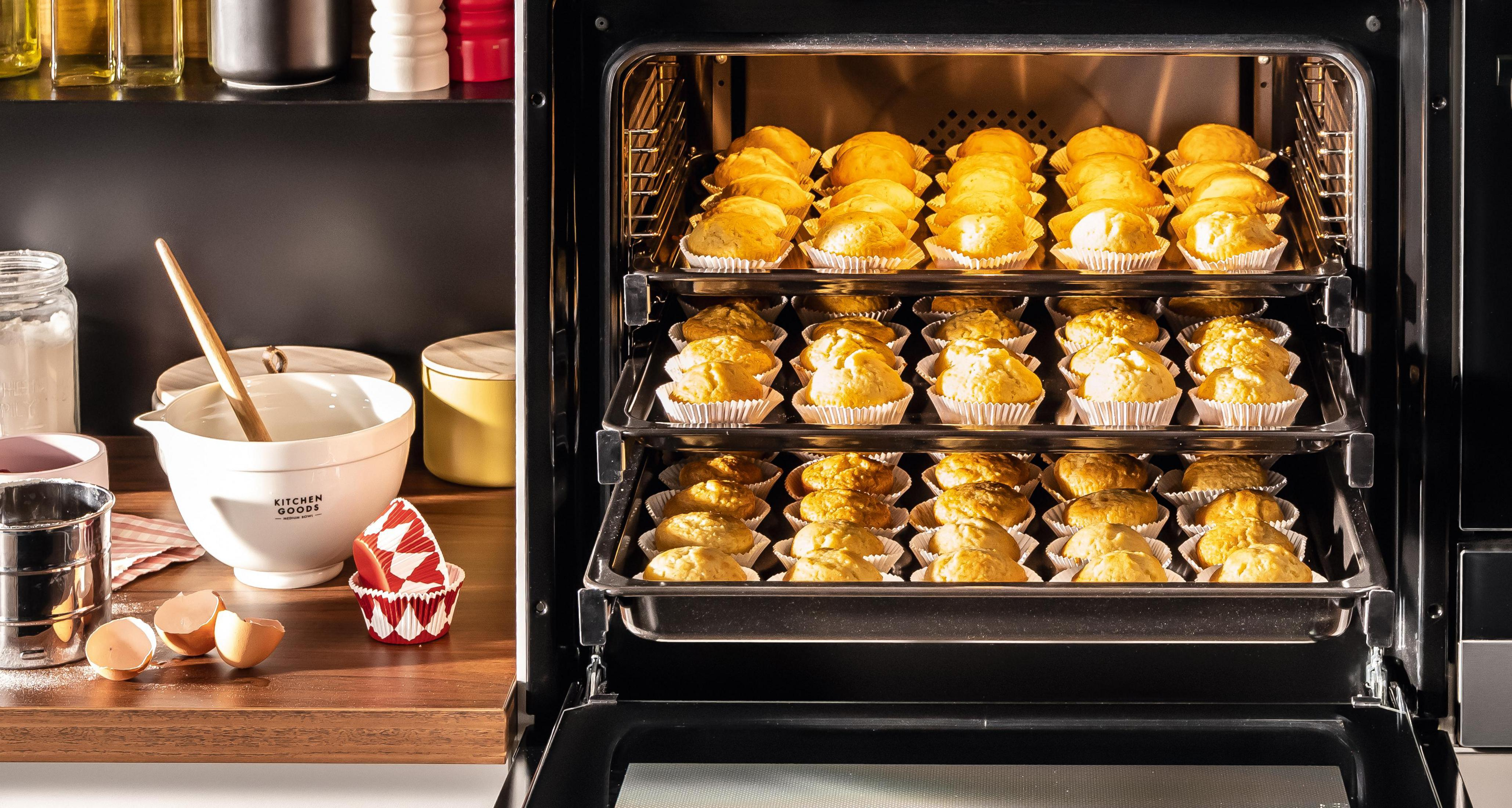 Ein Backofen mit mehreren Blechen Cupcakes, die zum Backen bereit sind.