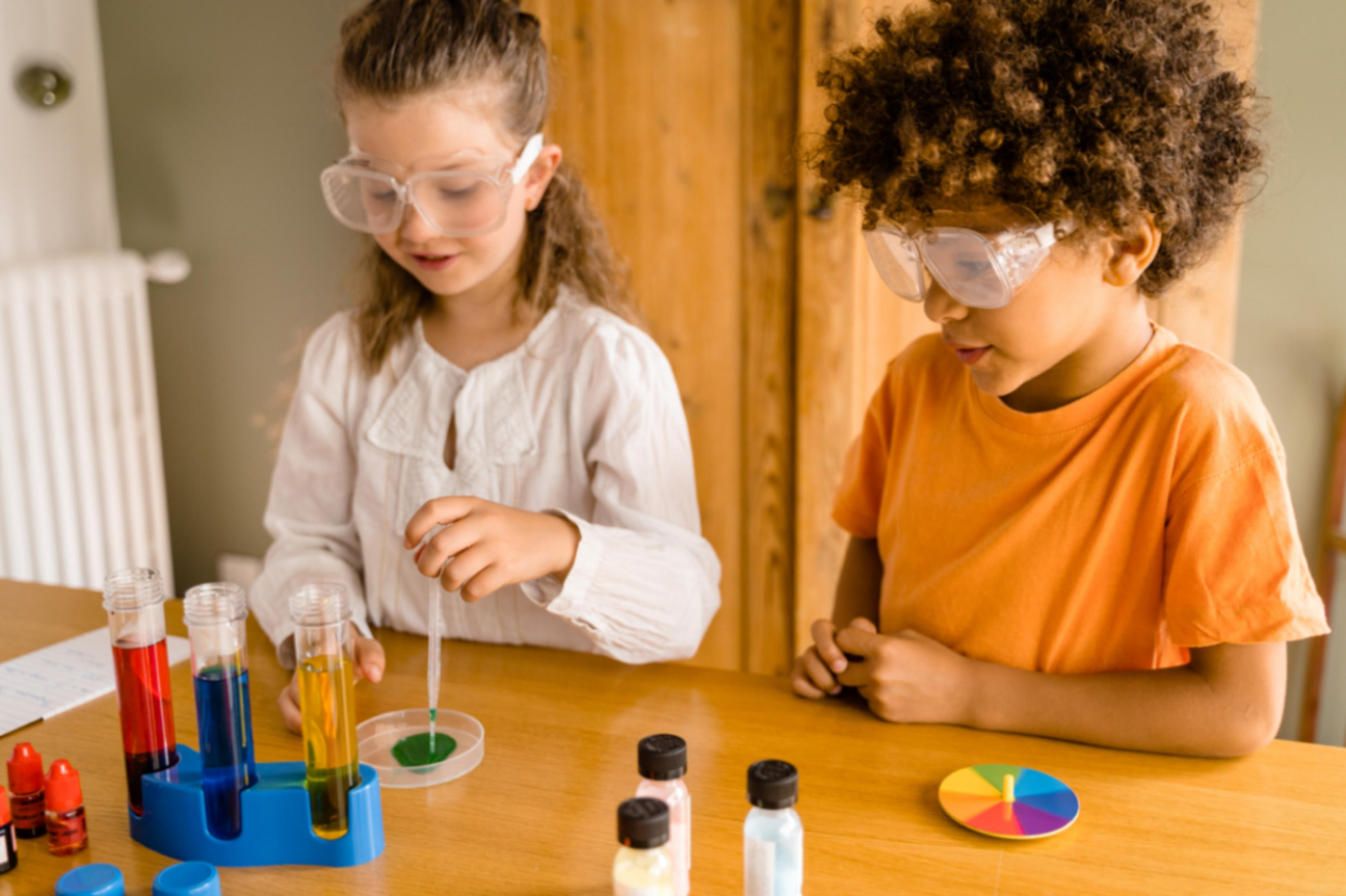 Zwei Kinder mit Schutzbrillen machen ein wissenschaftliches Experiment mit bunten Flüssigkeiten.