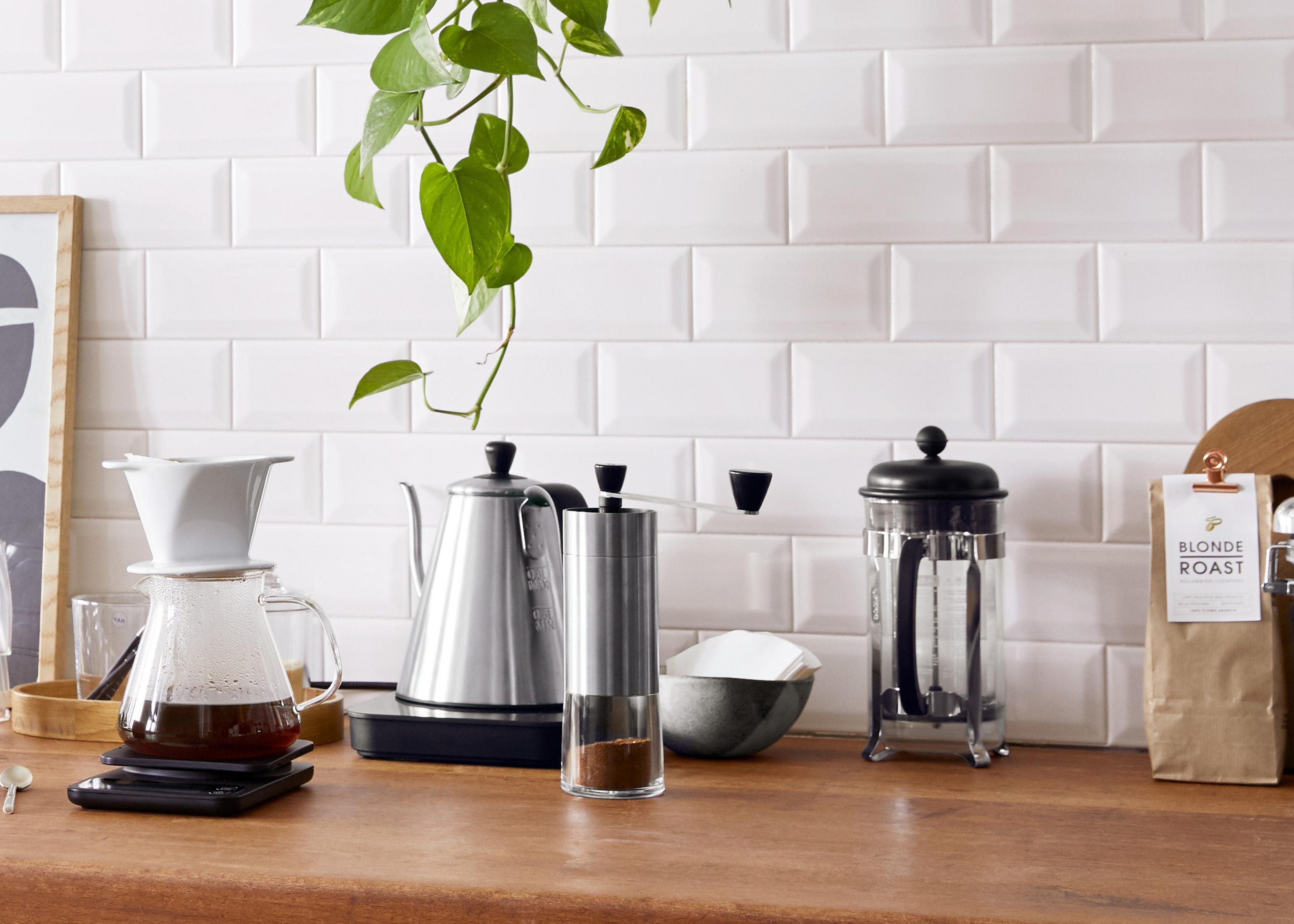 Kaffee-Setup auf einer Holz-Arbeitsplatte: Pour-Over, Wasserkocher, Mühle und French Press.