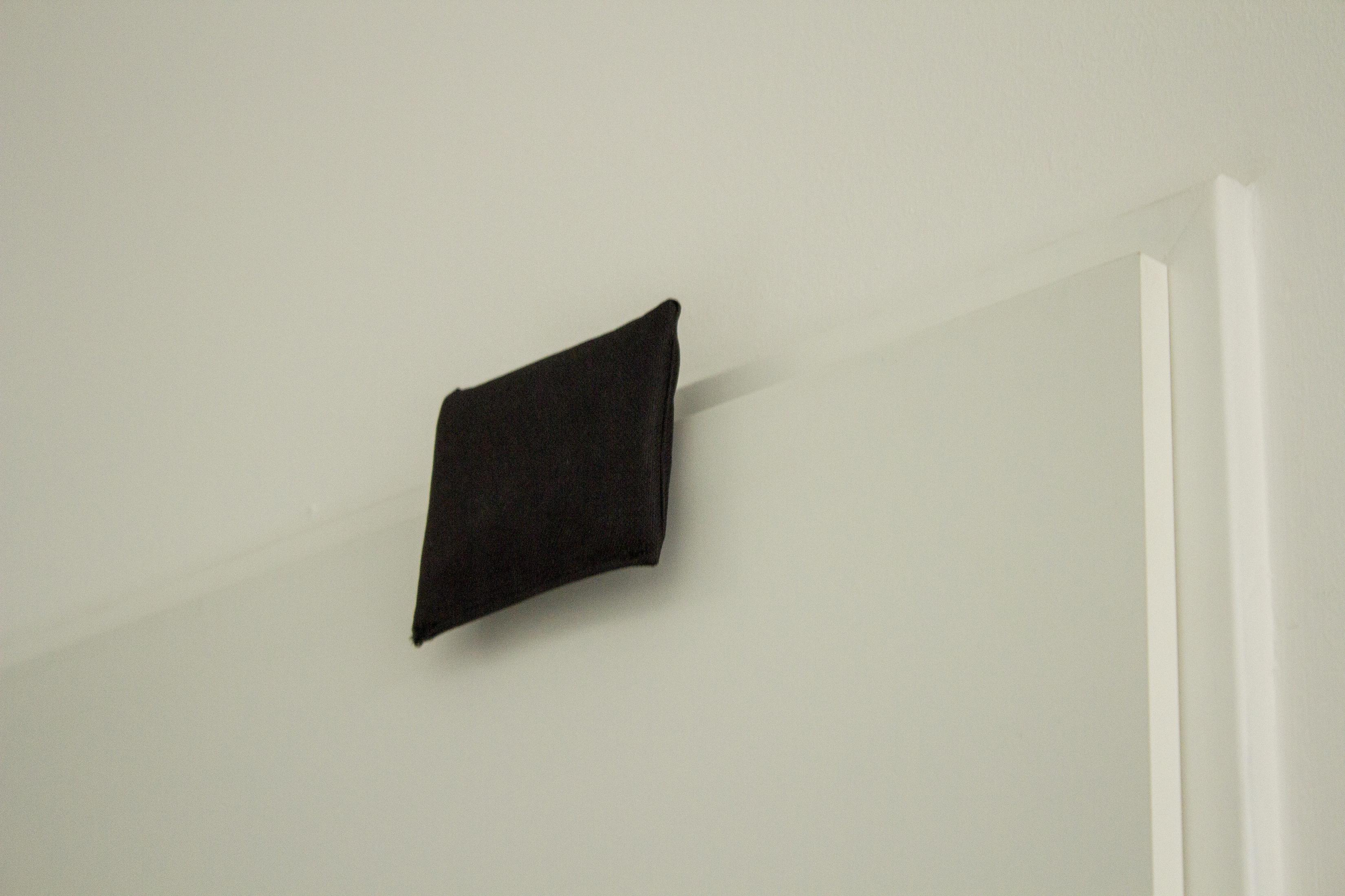 Quadrato di tessuto nero parzialmente su un muro bianco.