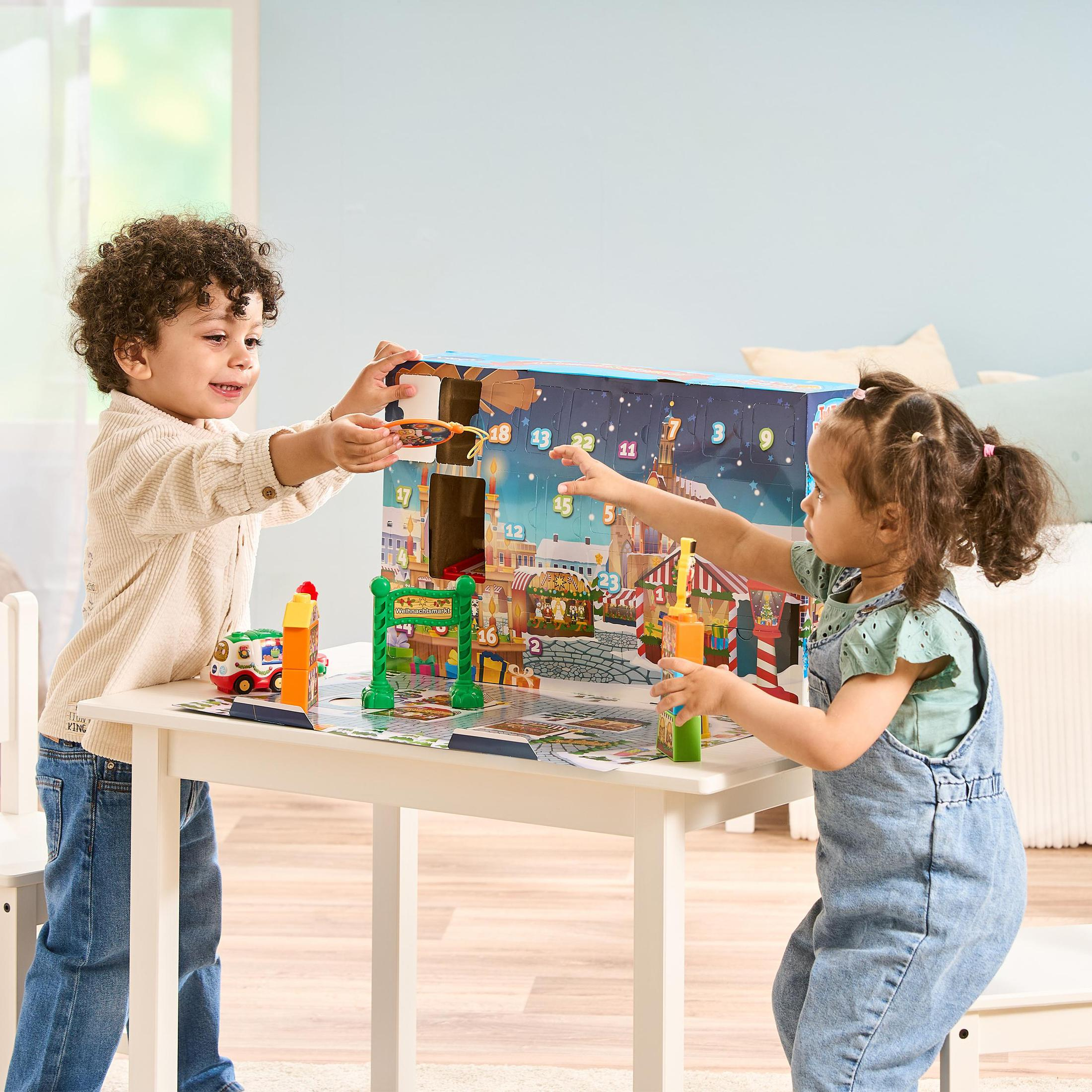 Zwei Kinder spielen mit einem Spielzeug-Adventskalender, mit einer Weihnachtsszene und bunten Spielzeugen.