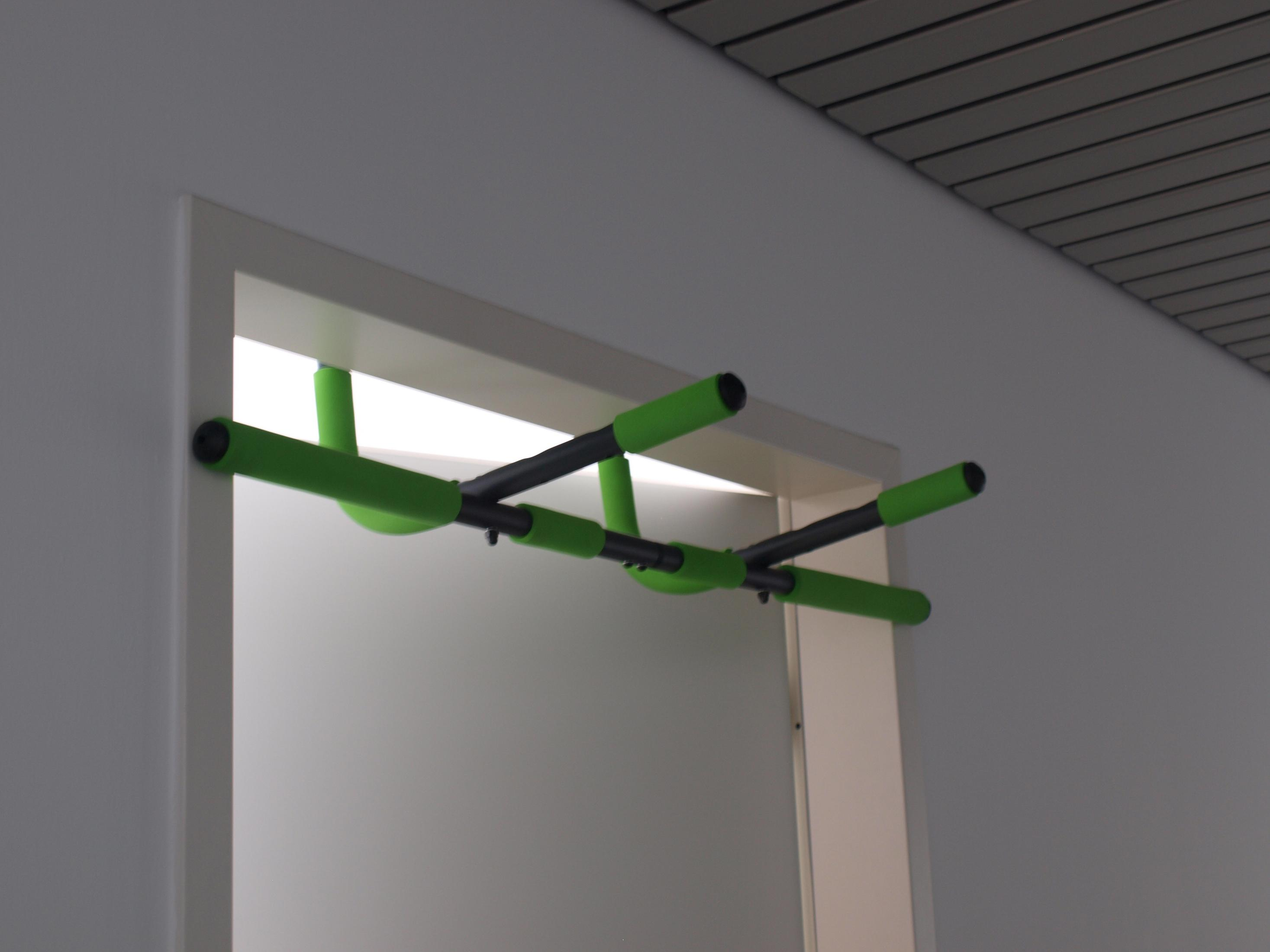 Una sbarra per trazioni verde e nera installata in un telaio di porta bianco.