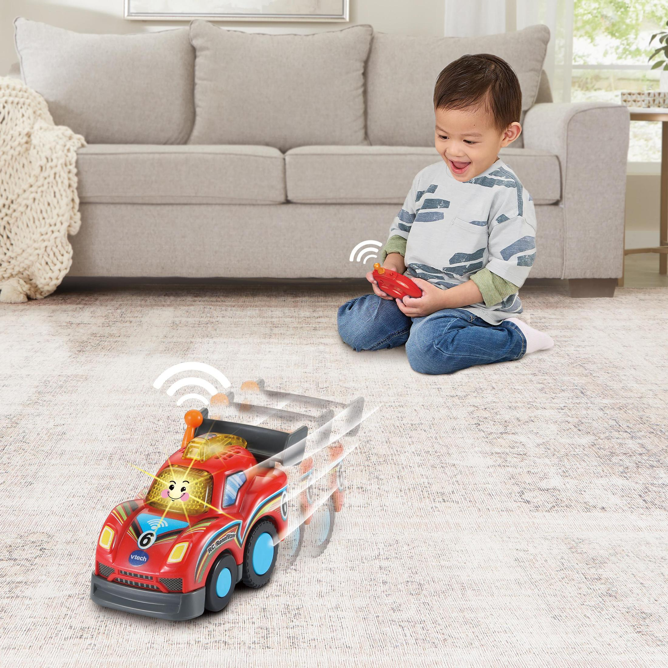Junge mit Spielzeugauto, lächelnd. Rotes Spielzeugauto bewegt sich. Beiger Teppich, weißes Sofa.