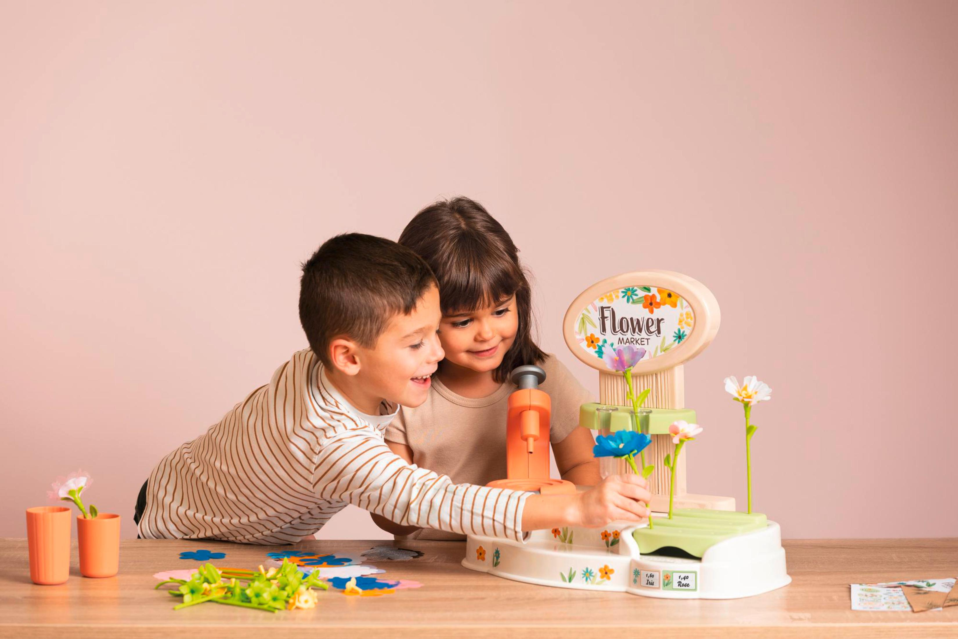 Zwei Kinder spielen mit einem Blumenmarktspielzeug. Rosa Hintergrund.