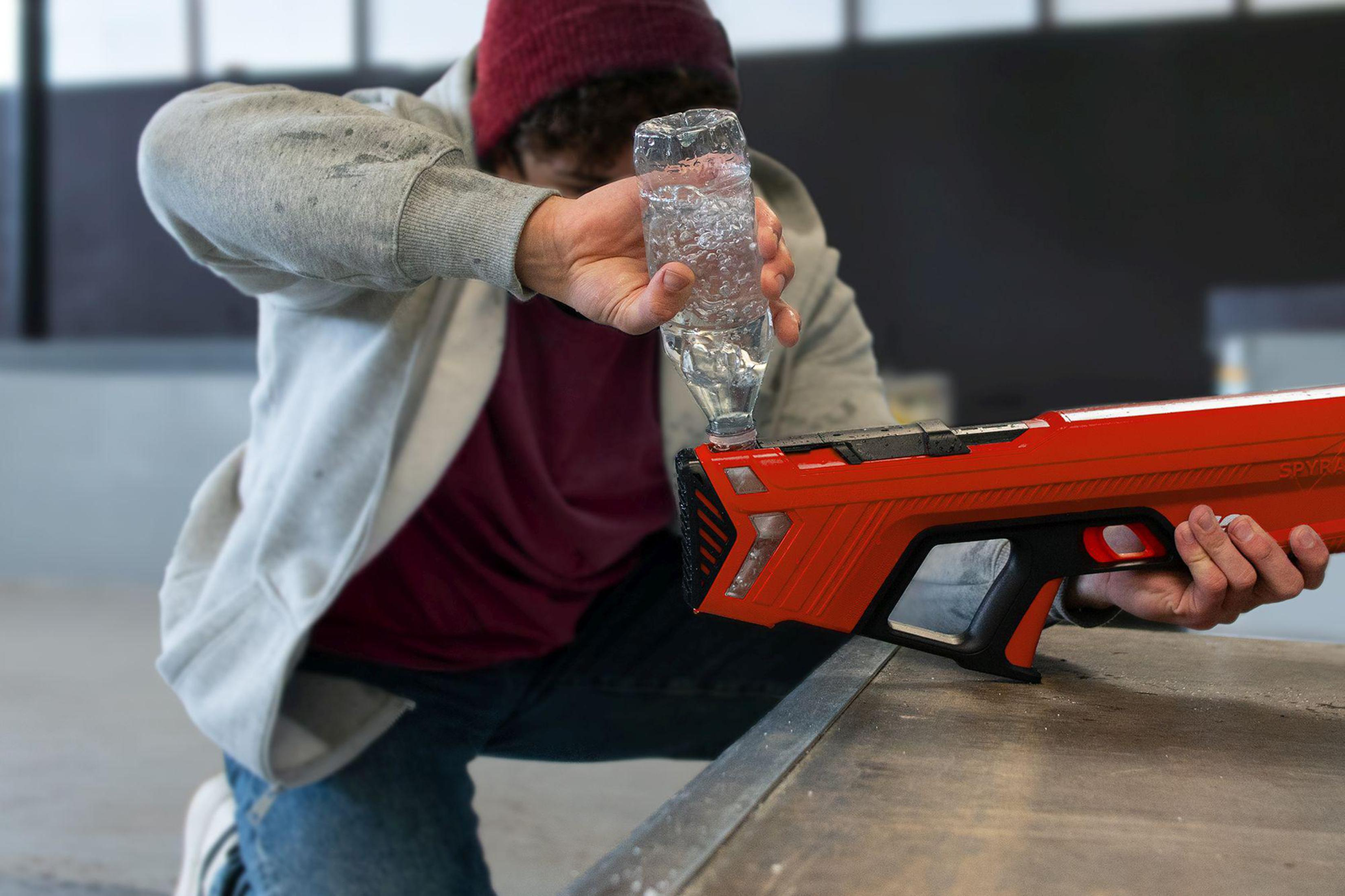 Eine Person gießt Wasser in eine rote Wasserpistole, auf einer Metalloberfläche.