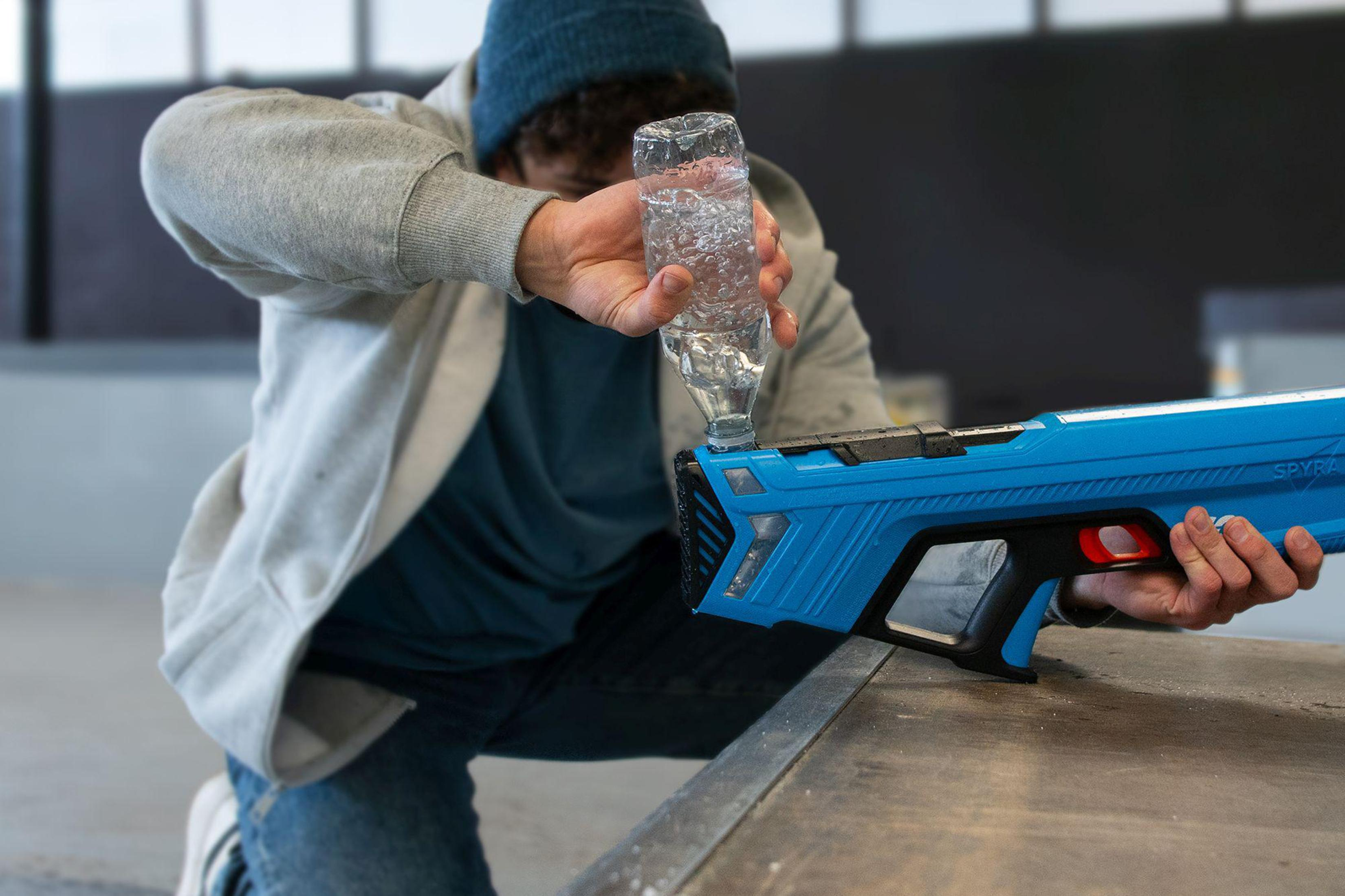 Ein Mann füllt eine blaue Spielzeugpistole mit Wasser aus einer Flasche.