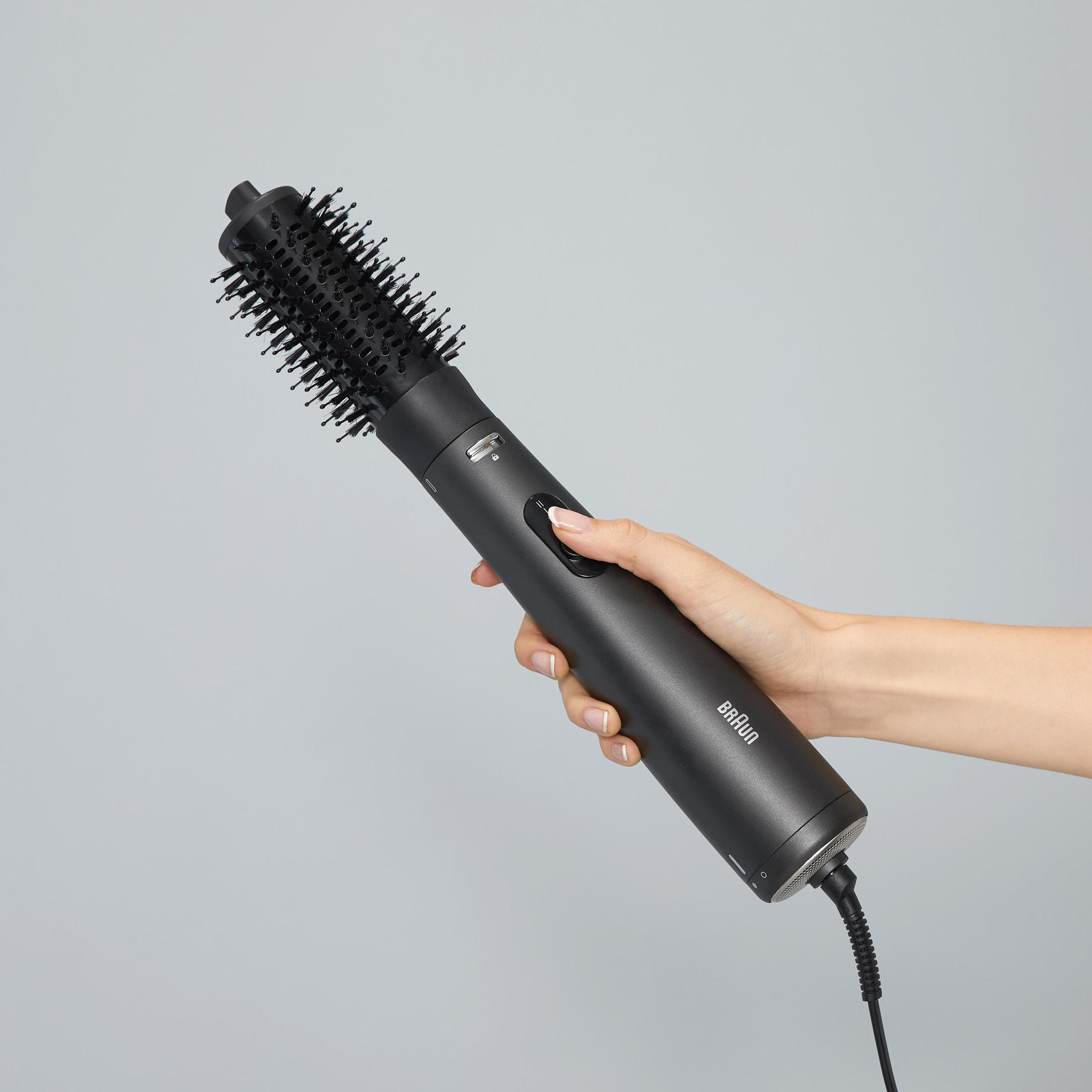 Una mano femminile che tiene un arricciacapelli Braun nero su sfondo grigio chiaro.