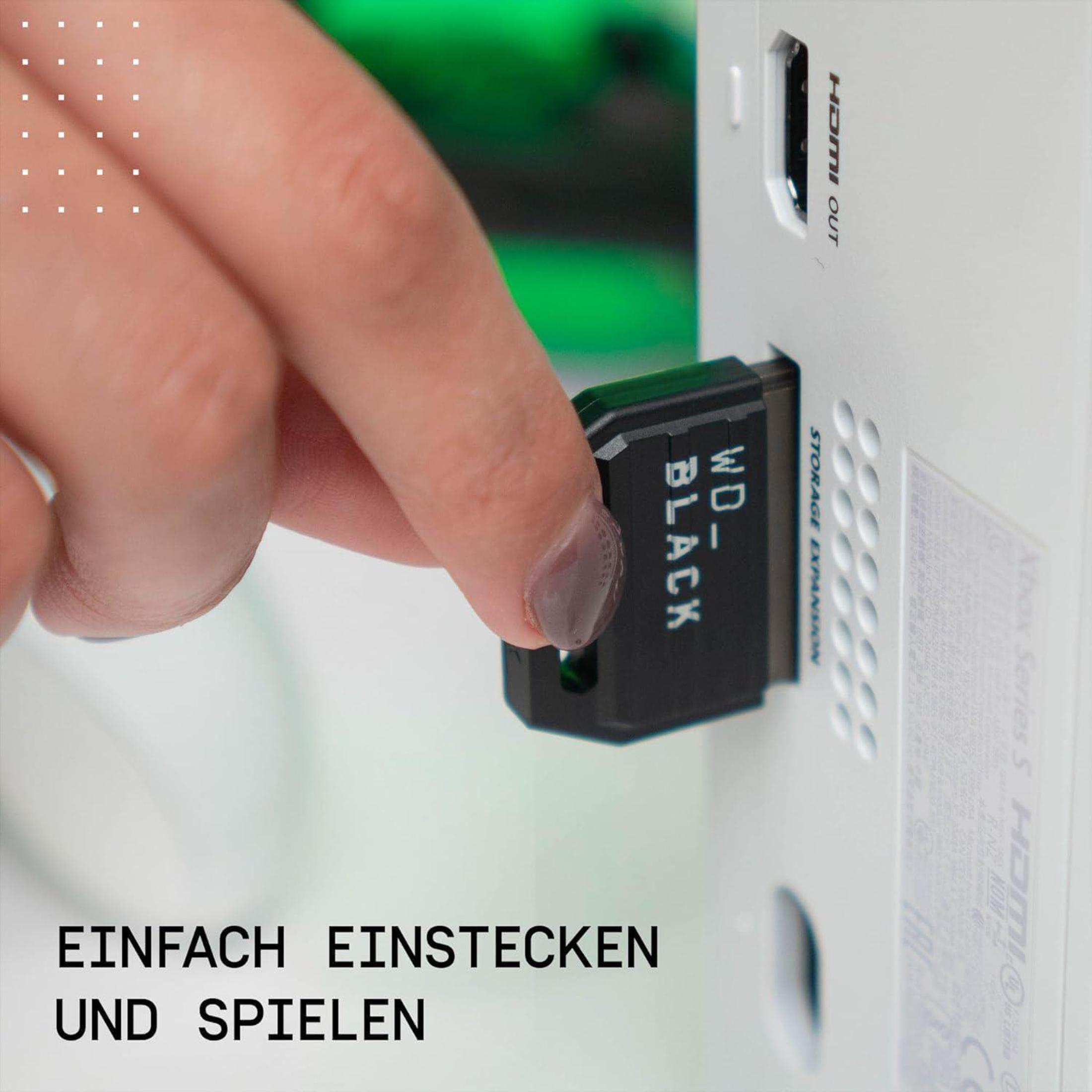 Eine Hand steckt eine schwarze Speichererweiterungskarte in die Xbox Series S Konsole. Text: 'WD BLACK'.
