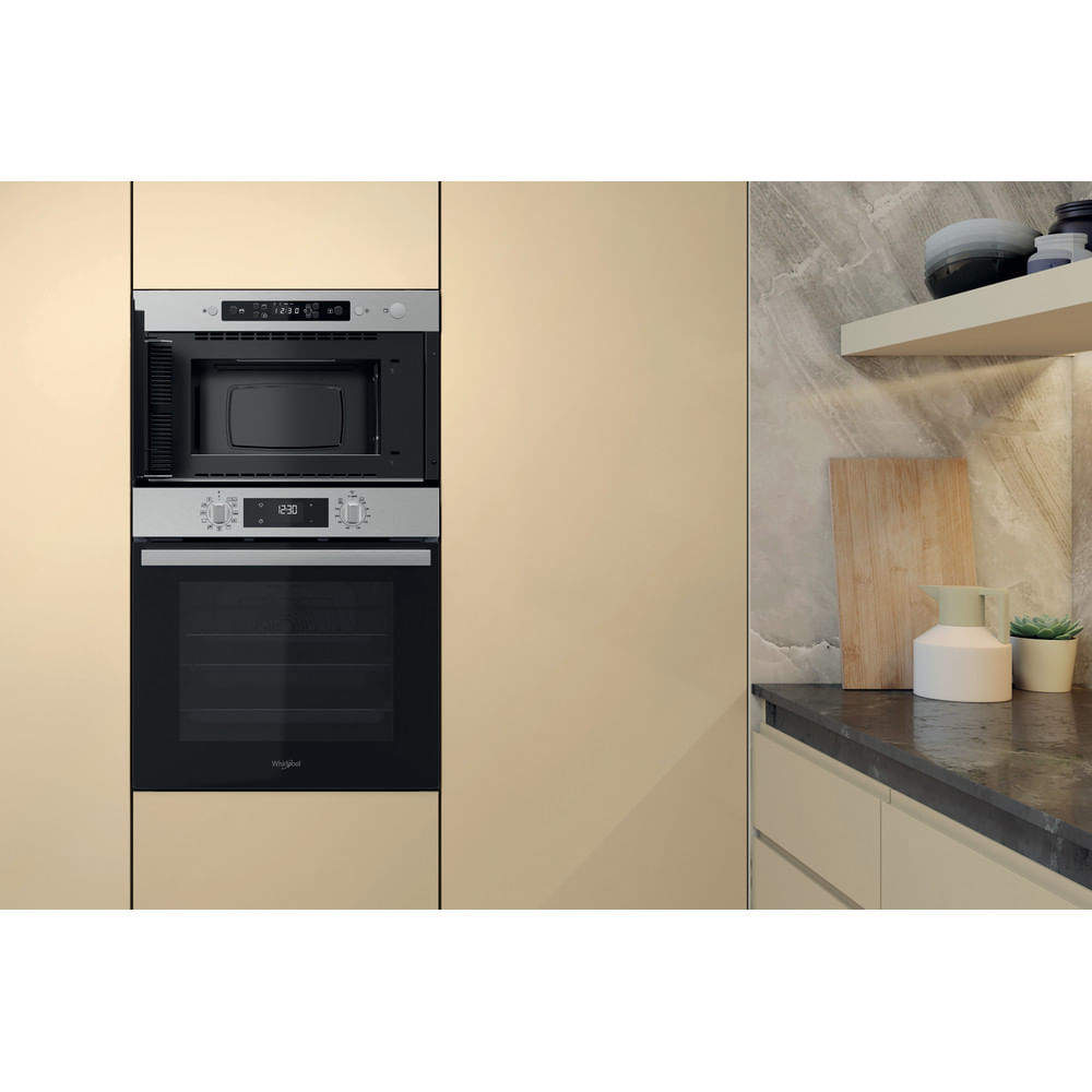 Combinazione microonde e forno a incasso. Armadi beige circondano gli elettrodomestici. Un bancone con decorazioni è a destra.