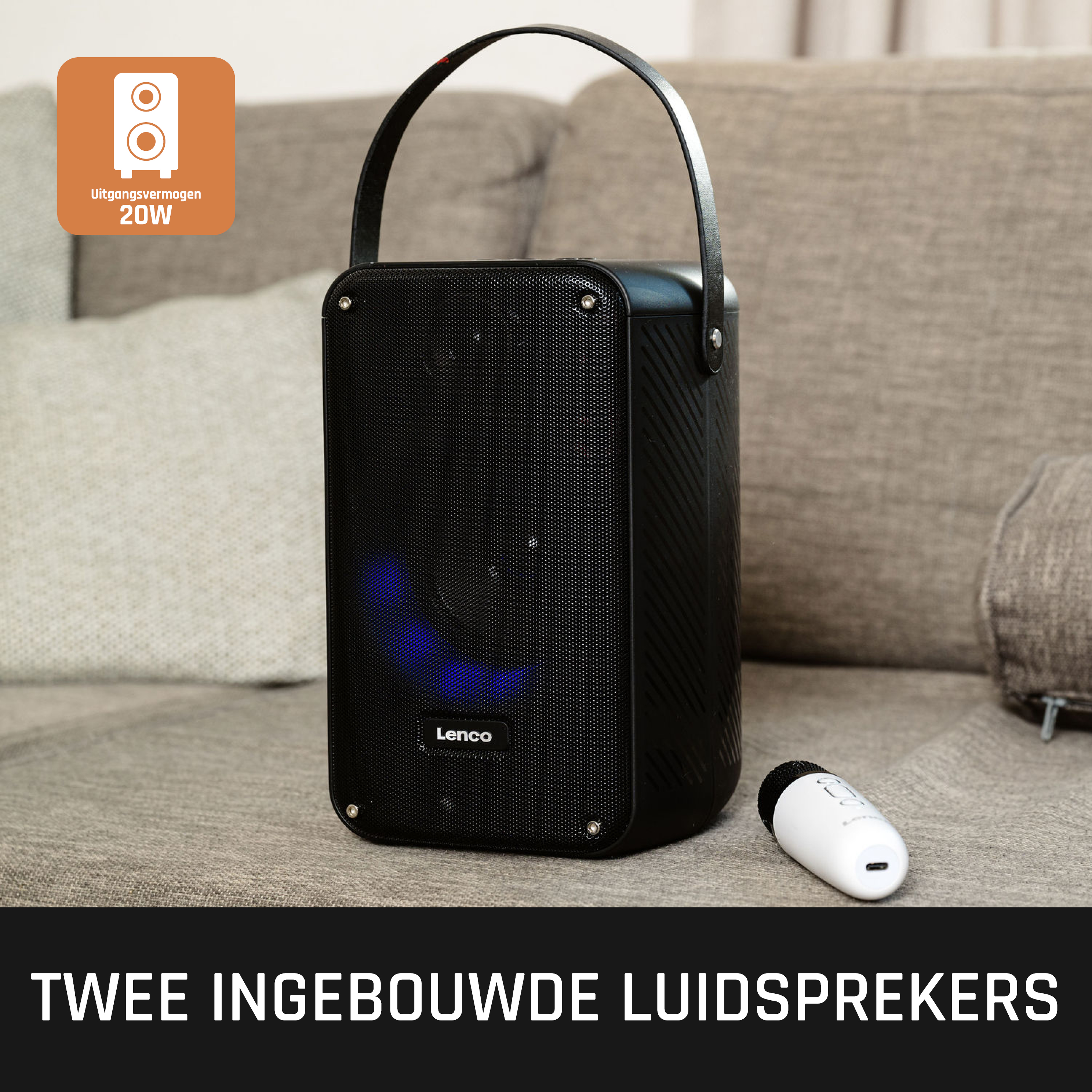 Zwarte draagbare luidspreker met handvat en afstandsbediening, tegen een bank, Nederlandse tekst.