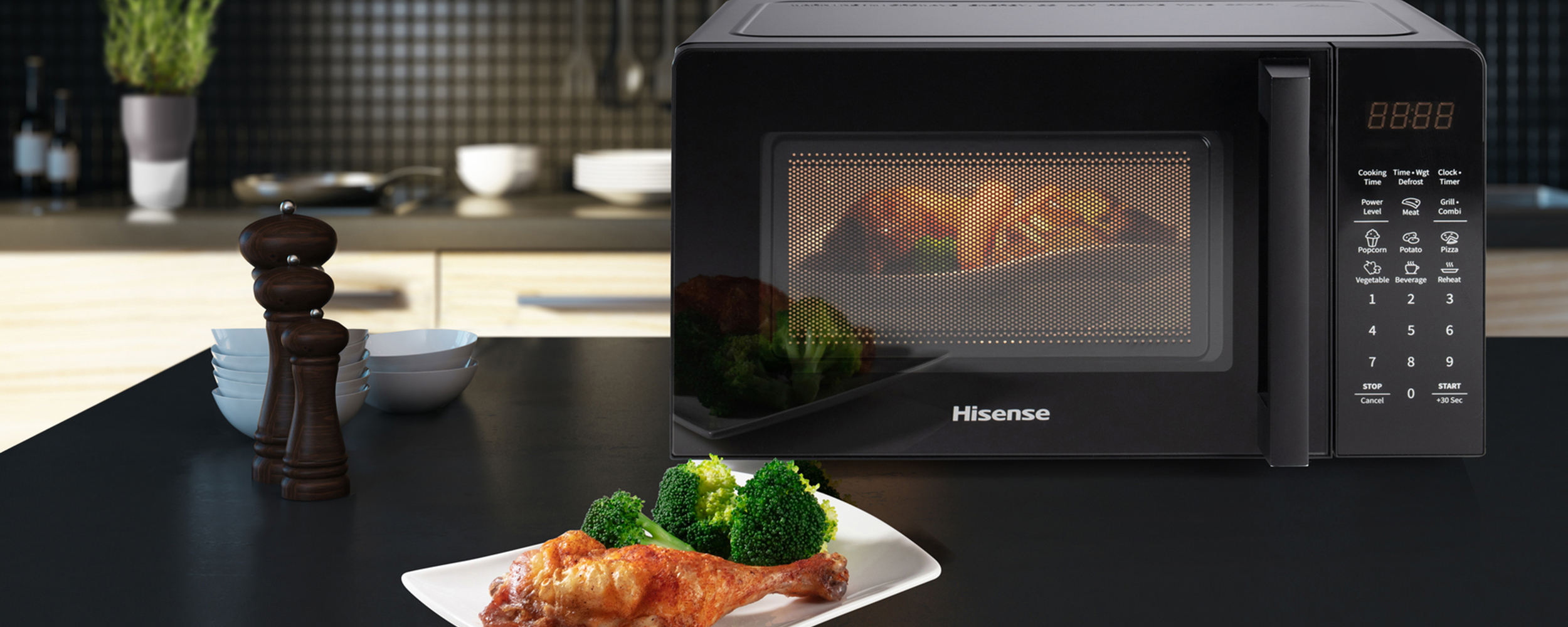 Microonde Hisense su superficie nera. Piatto con pollo e broccoli. Sfondo cucina con piastrelle nere.