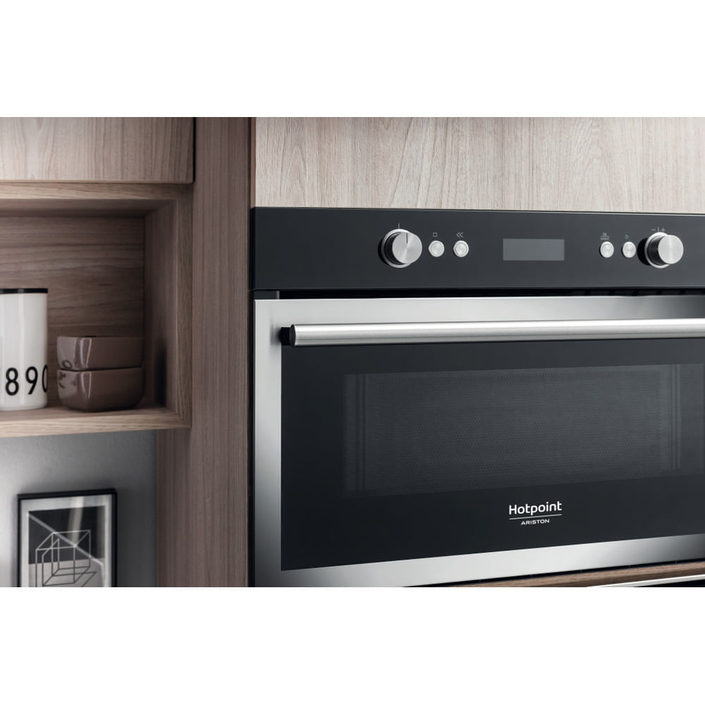 Forno a microonde nero incassato in mobili di legno. Logo Hotpoint Ariston visibile.