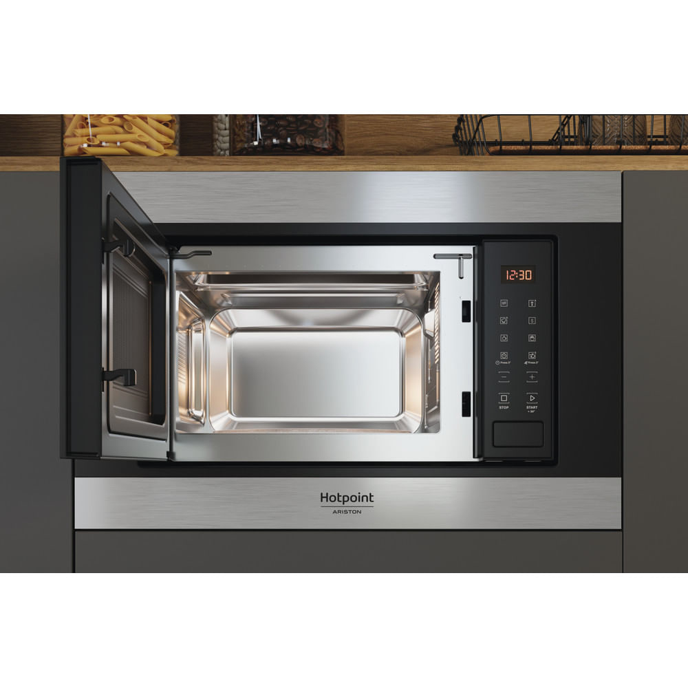 Forno a microonde con porta aperta, che mostra l'interno. Il marchio è Hotpoint Ariston. Lo sfondo è una cucina.