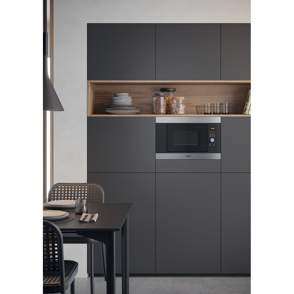 Scena cucina moderna con mobili scuri. Forno a microonde da incasso. Mensola in legno con piatti e barattoli.