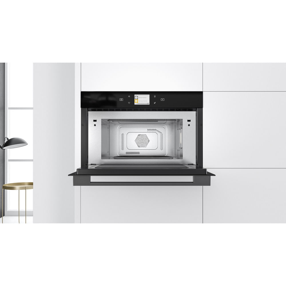 Forno a microonde nero aperto incassato in una parete bianca. Interno visibile.