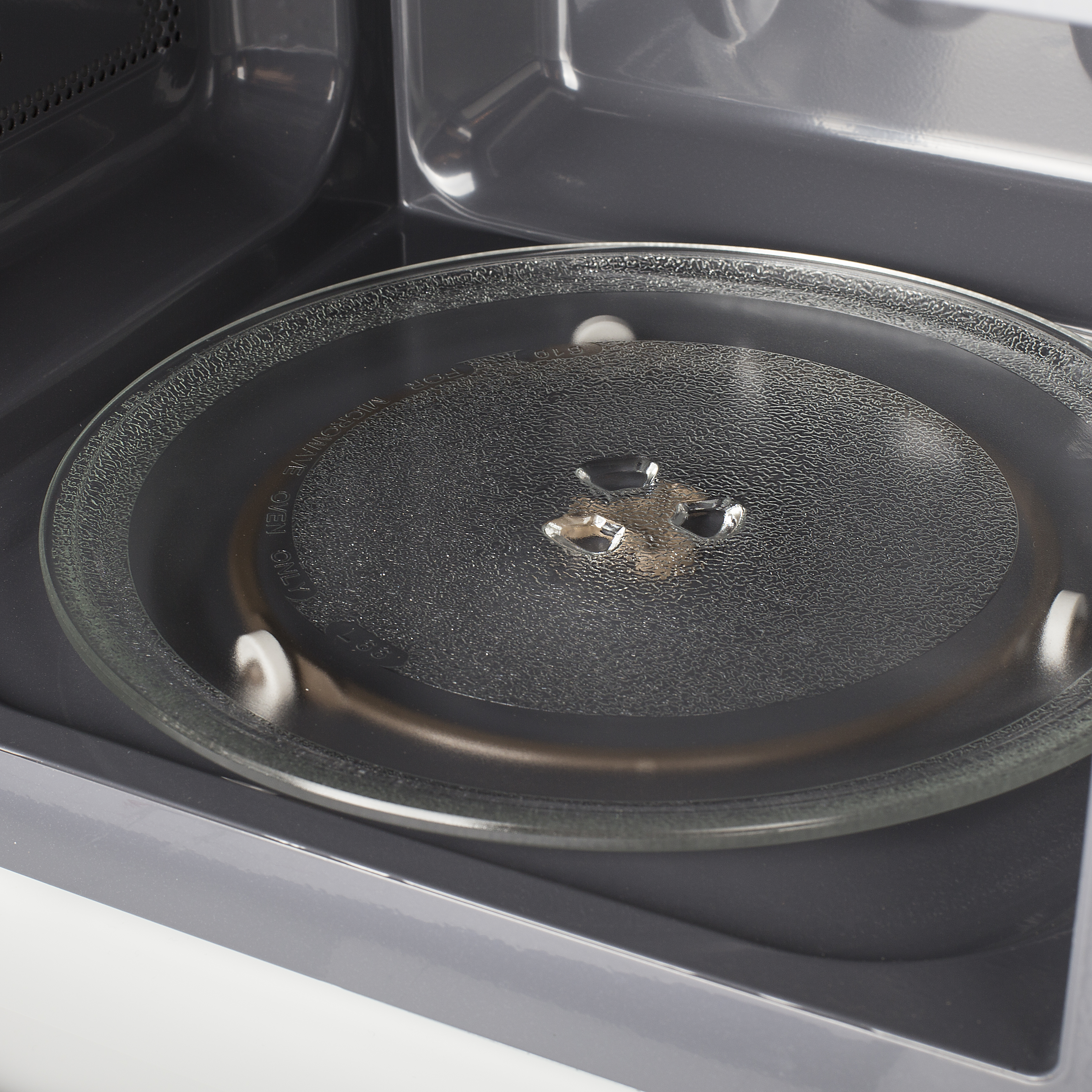 Zbliżenie wnętrza kuchenki mikrofalowej. Szklany talerz jest ostry, wspierany przez białe rolki.