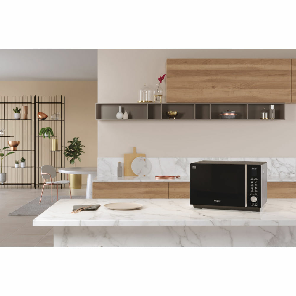Microondas Whirlpool negro sobre encimera de mármol blanco. Escena de cocina con elementos beige y madera.