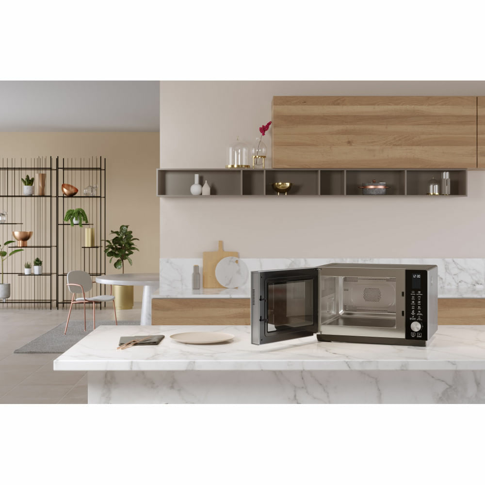 Horno microondas sobre encimera blanca, con puerta abierta, y vista de la cocina.