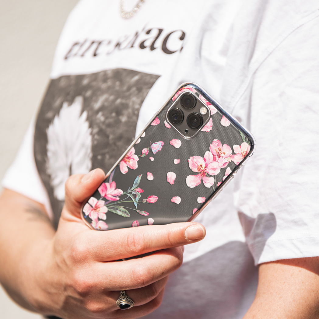 Persona che tiene in mano un telefono con una custodia dal design floreale rosa; lo sfondo è chiaro.