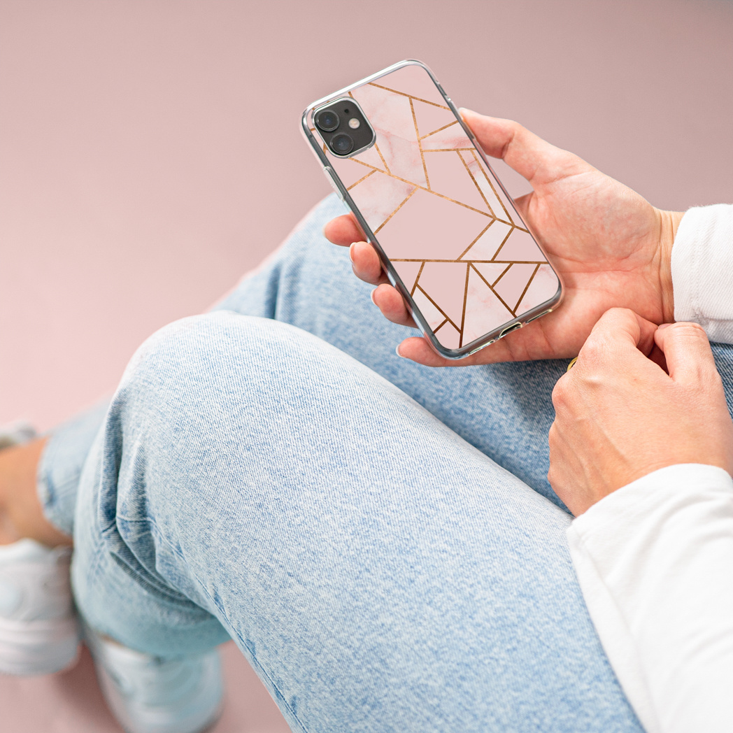 Persoon houdt een telefoon met een roze en gouden patroonhoes vast, draagt een blauwe jeans.