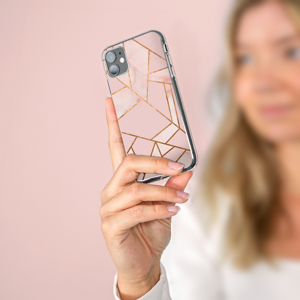 Vrouw houdt telefoon vast met roze marmer en gouden geometrisch patroon. De telefoon is scherp.