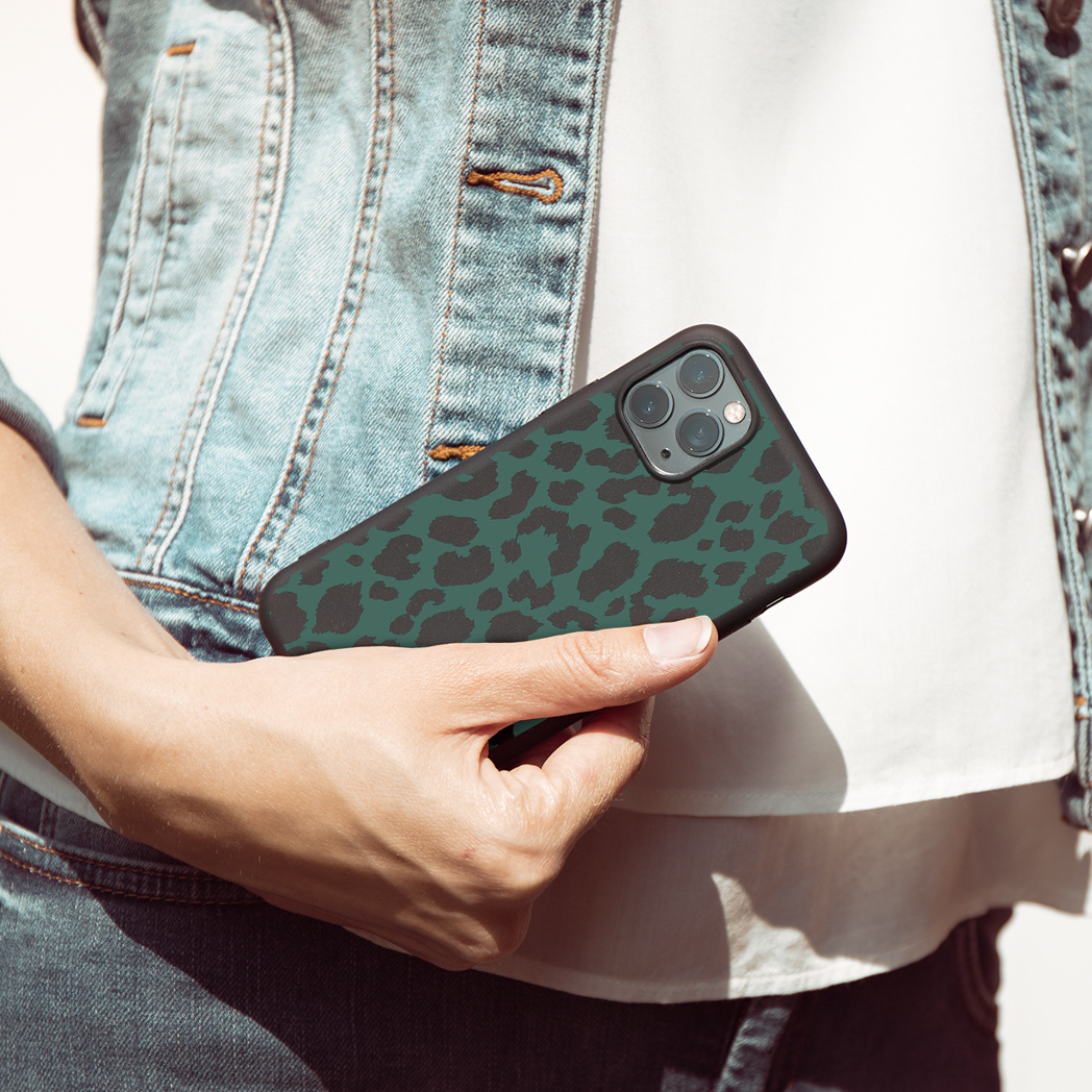 Persona che tiene una custodia con stampa animalier verde su giacca di jeans.