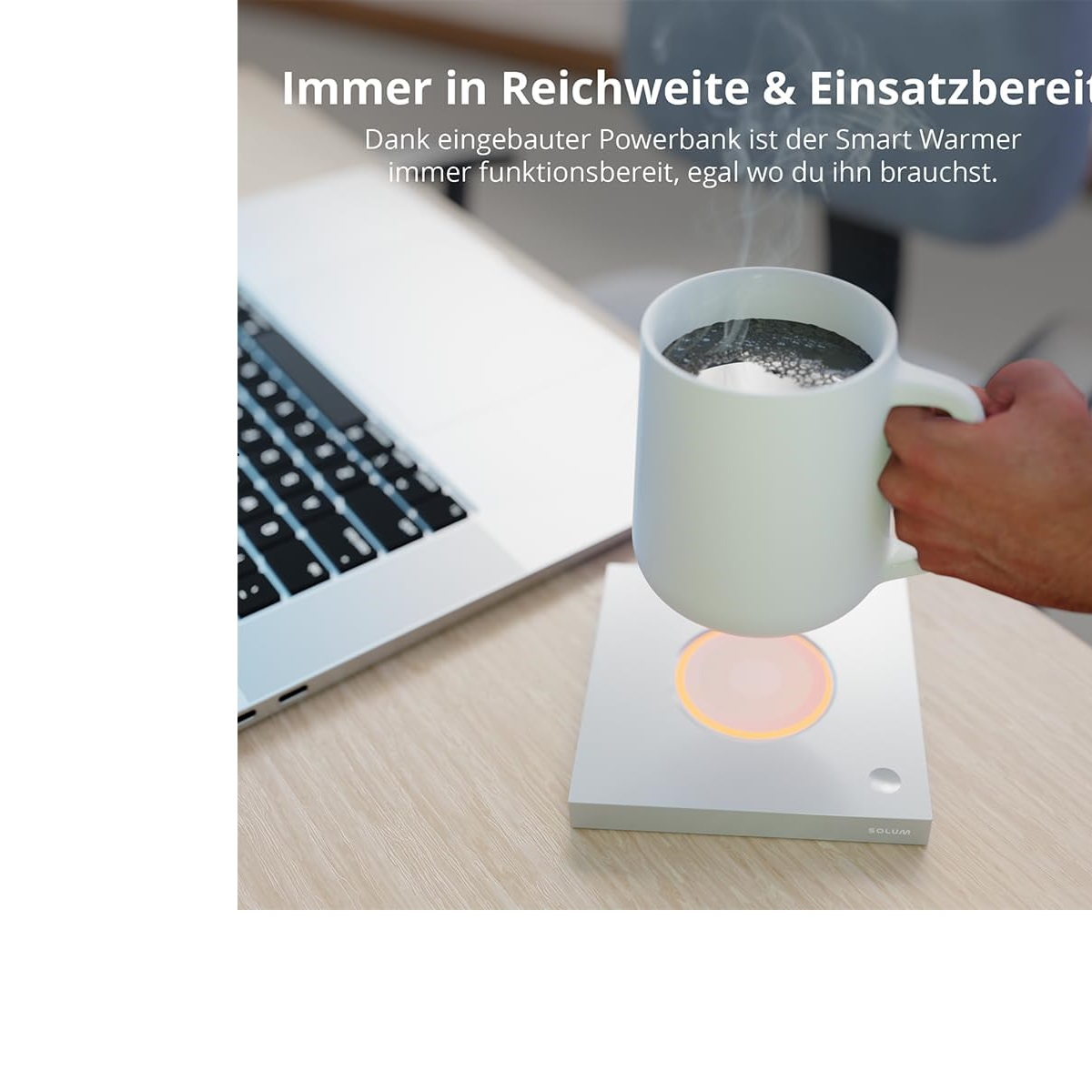 Eine Hand, die einen weißen Becher auf einer Heizbasis vor einem Laptop hält.