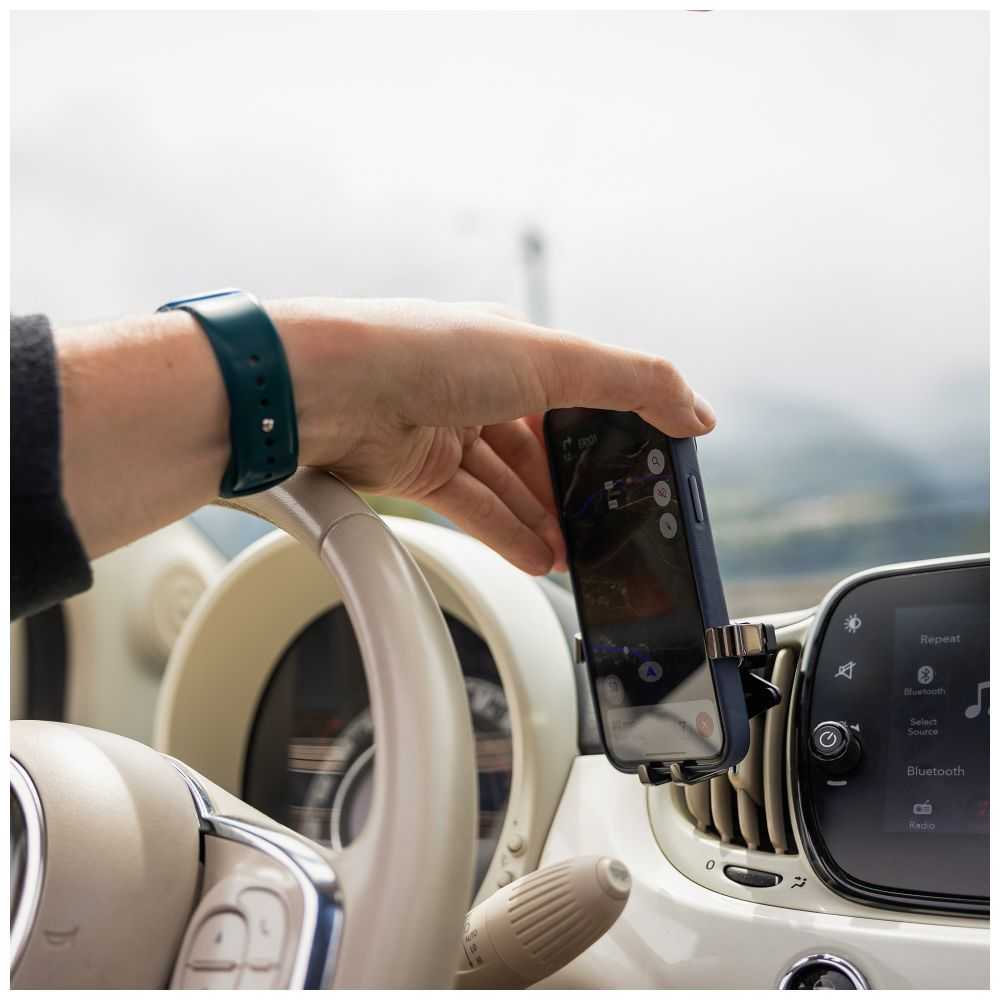 Hand hält Handy mit Karte, befestigt an einer Lüftung im Auto.