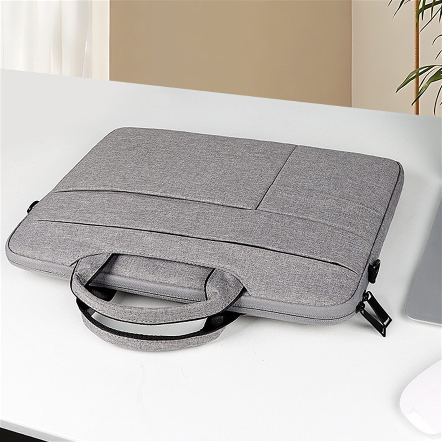 Graue Laptoptasche mit Henkel und Reißverschluss auf weißem Tisch.