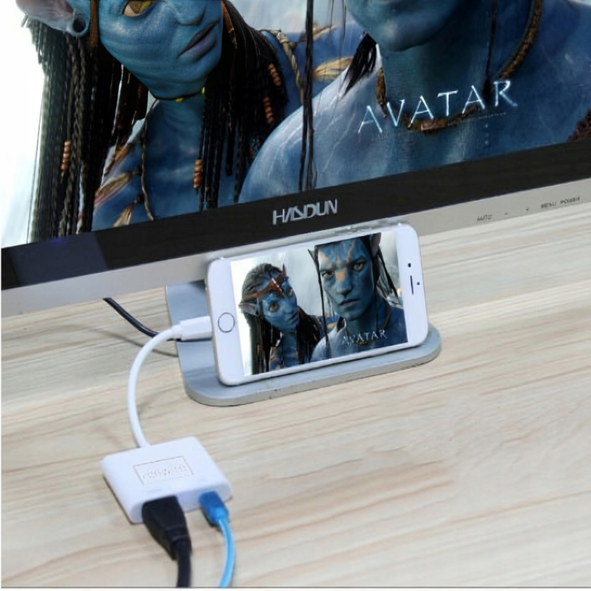 Telefon wyświetlający film 'Avatar', podłączony do urządzenia, przed ekranem telewizora z obrazem Avatara.