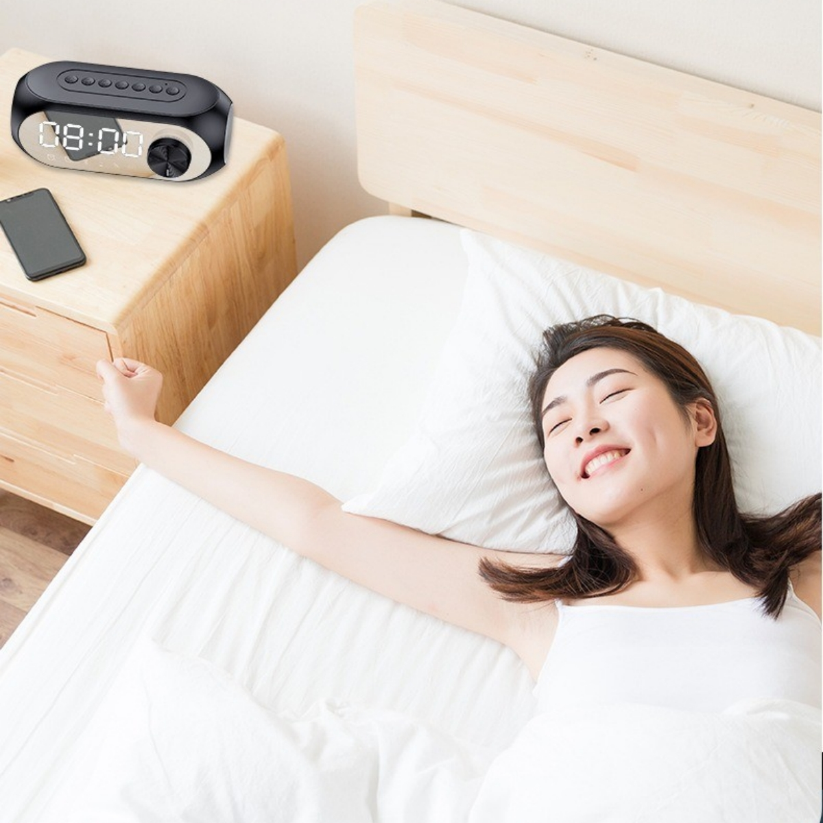 Das Bild zeigt eine Frau im Bett mit einer Digitaluhr und einem Smartphone auf dem Nachttisch.