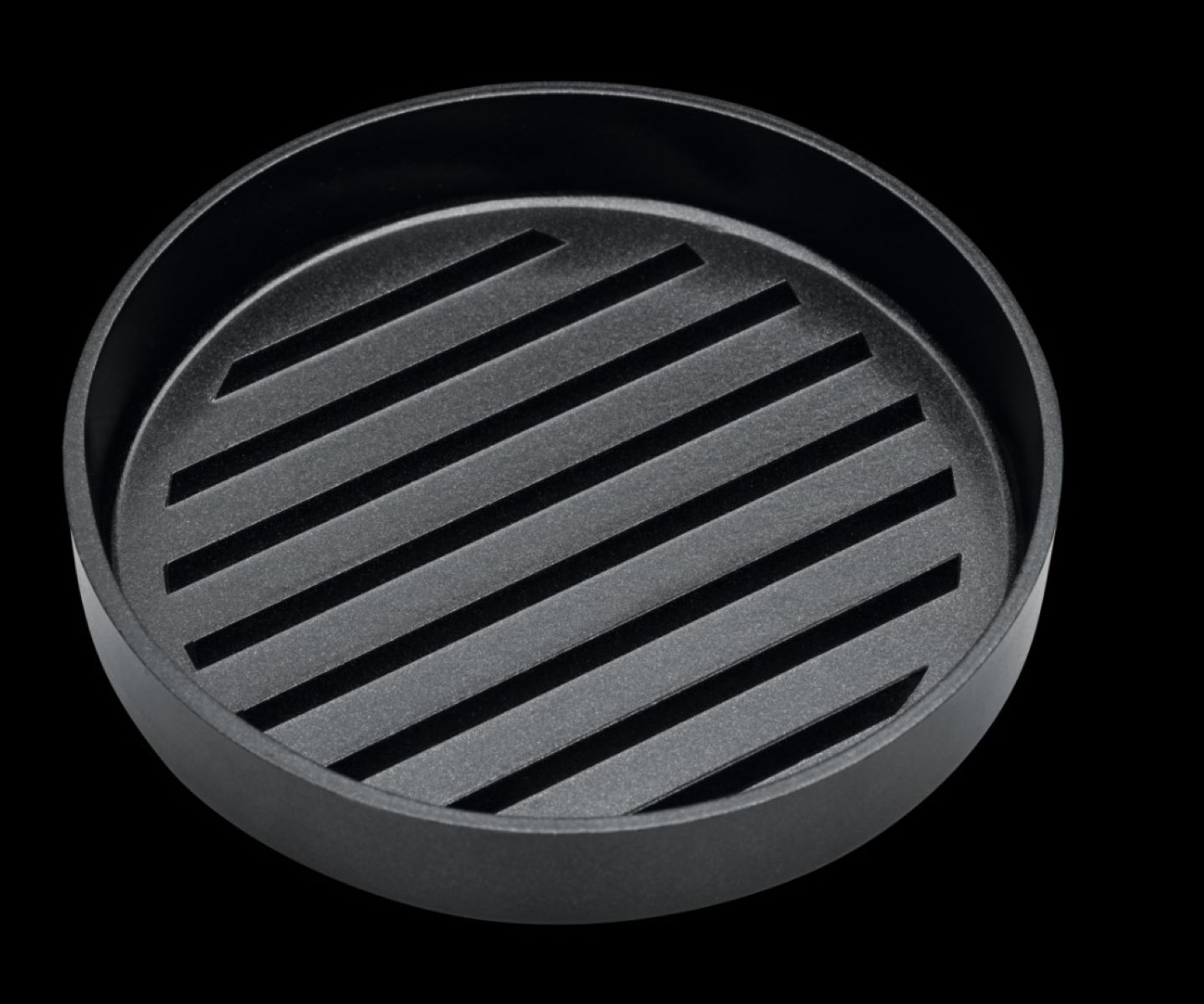 Eine schwarze, runde Grillpfanne mit parallelen Rillen. Der Hintergrund ist tiefschwarz.