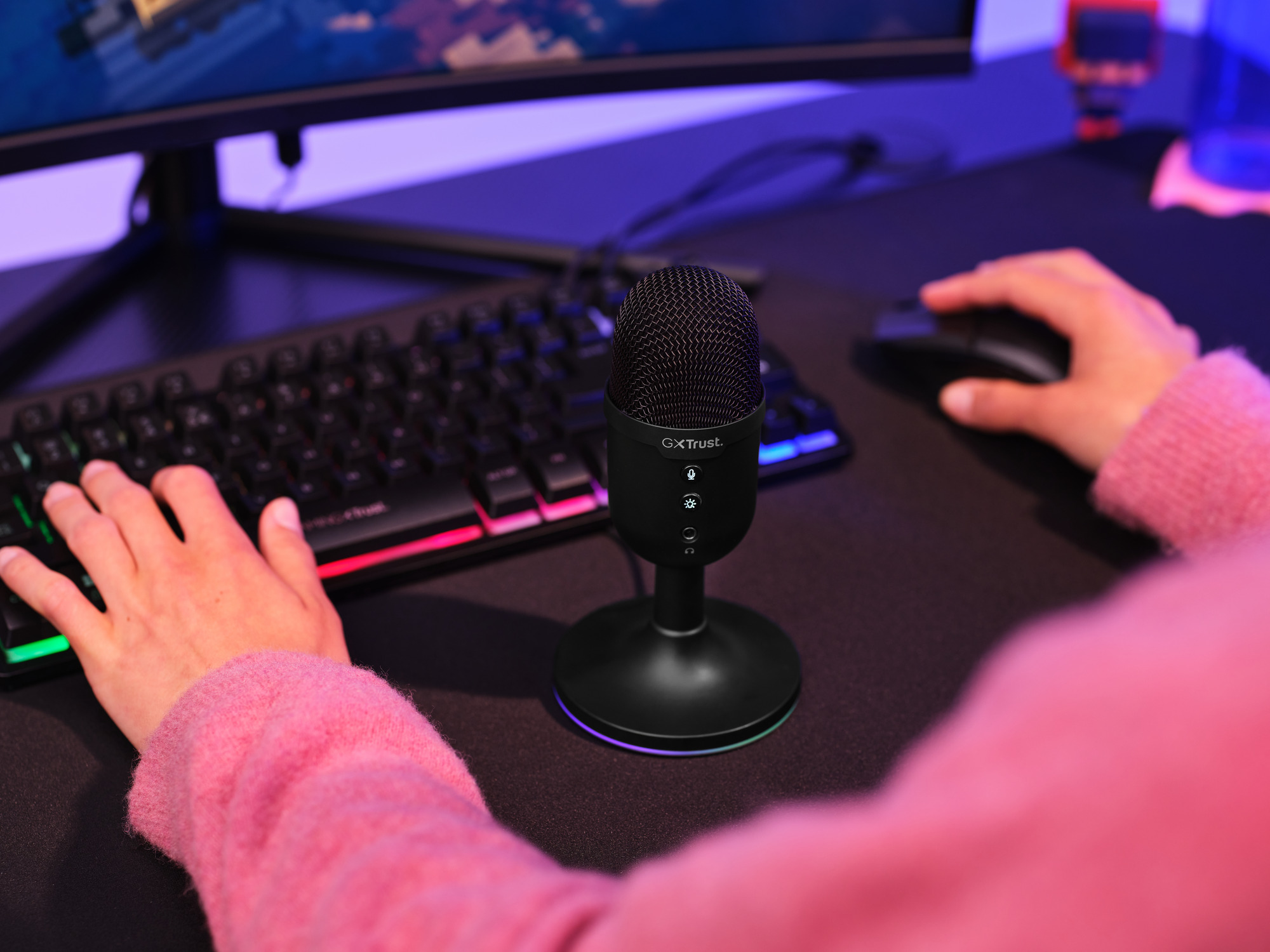 Eine Person mit rosa Ärmeln, die ein schwarzes Mikrofon und eine Tastatur verwendet, mit einem Computerbildschirm im Hintergrund.
