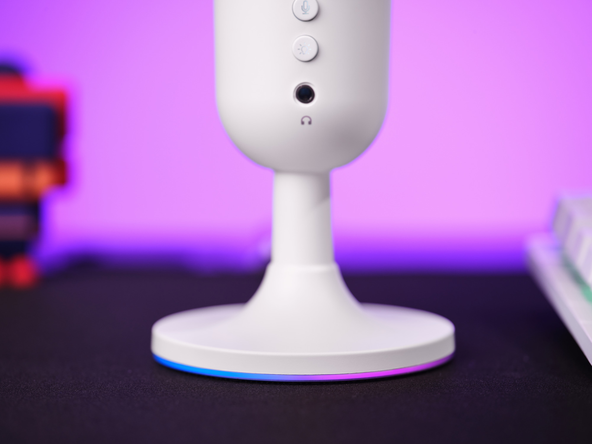 Witte microfoon met knoppen, een zwarte knop en een koptelefoonaansluiting. De basis heeft een kleurrijke gloed.