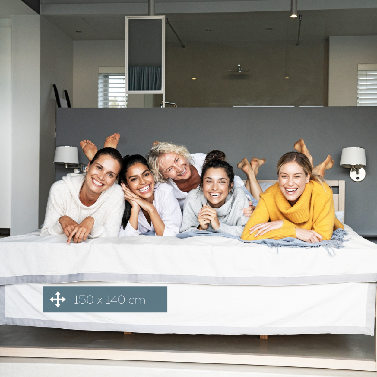 Grupo de cinco mujeres acostadas en una cama, sonriendo a la cámara, con un letrero.